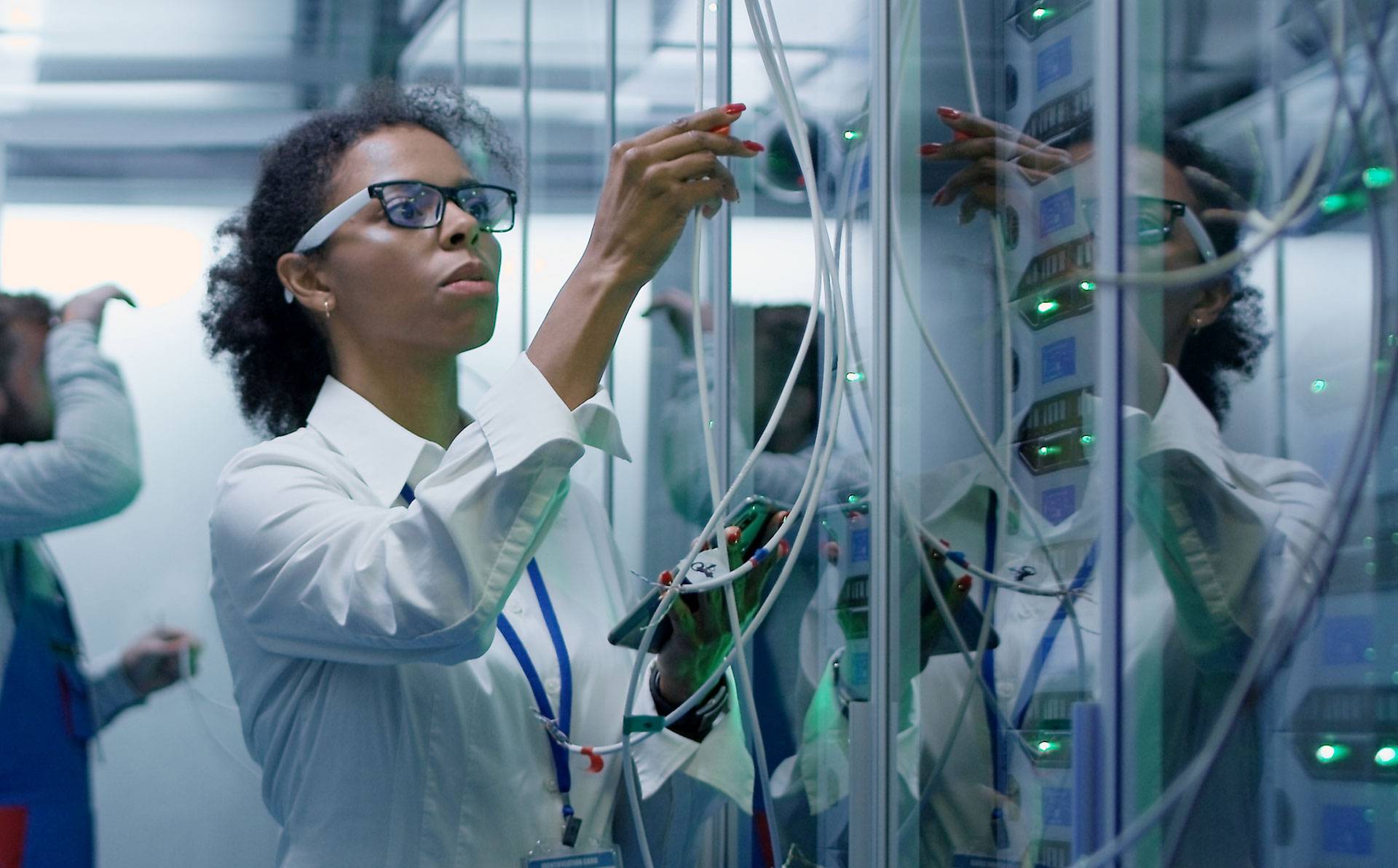 A woman holds cables that go to a computer server.