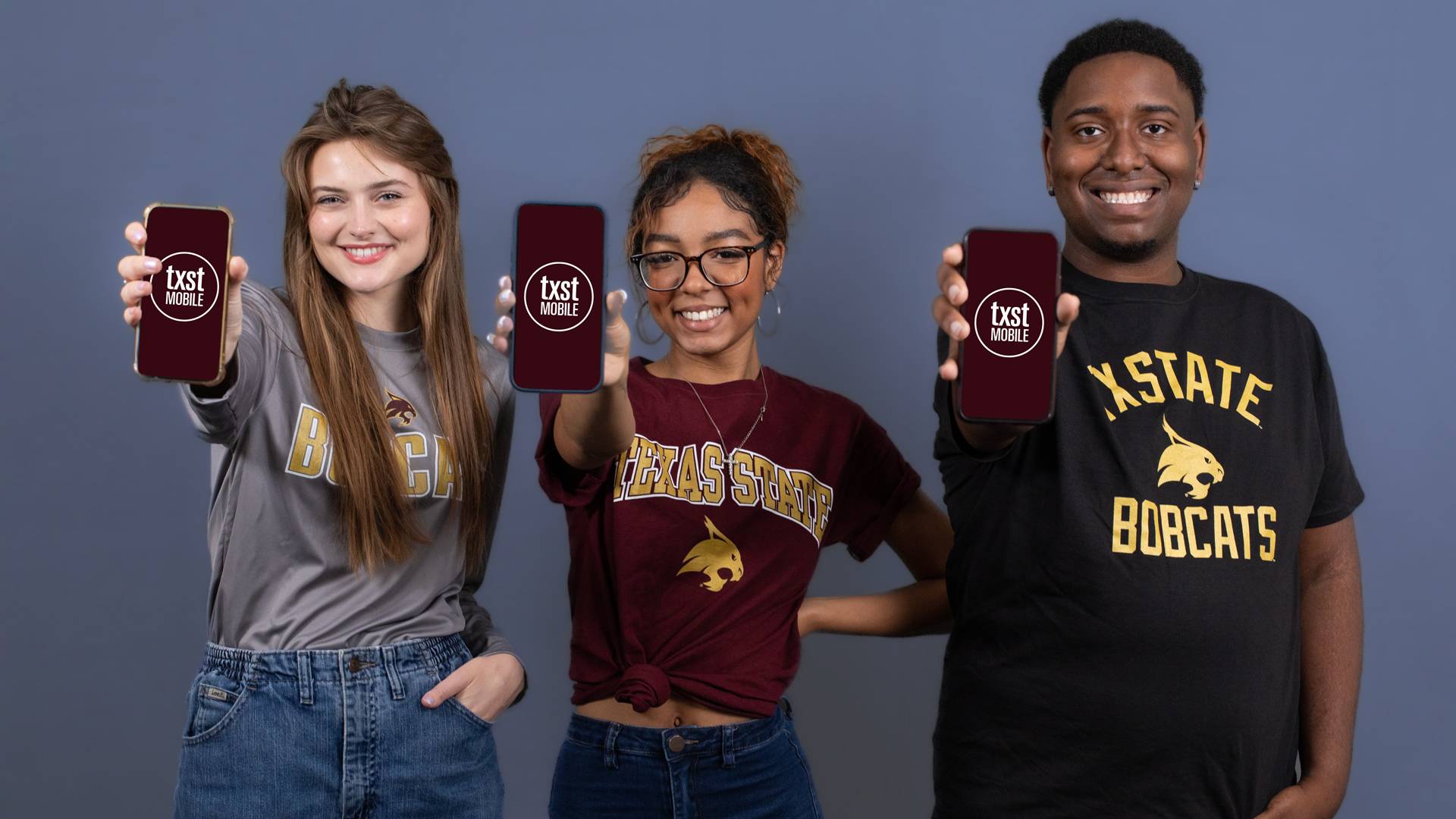 Three students holding mobile devices showing the TXST Mobile logo on the screens.