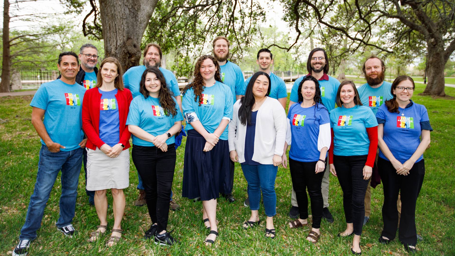 A dozen members of Texas State’s Mobile Web Team stand outside under trees