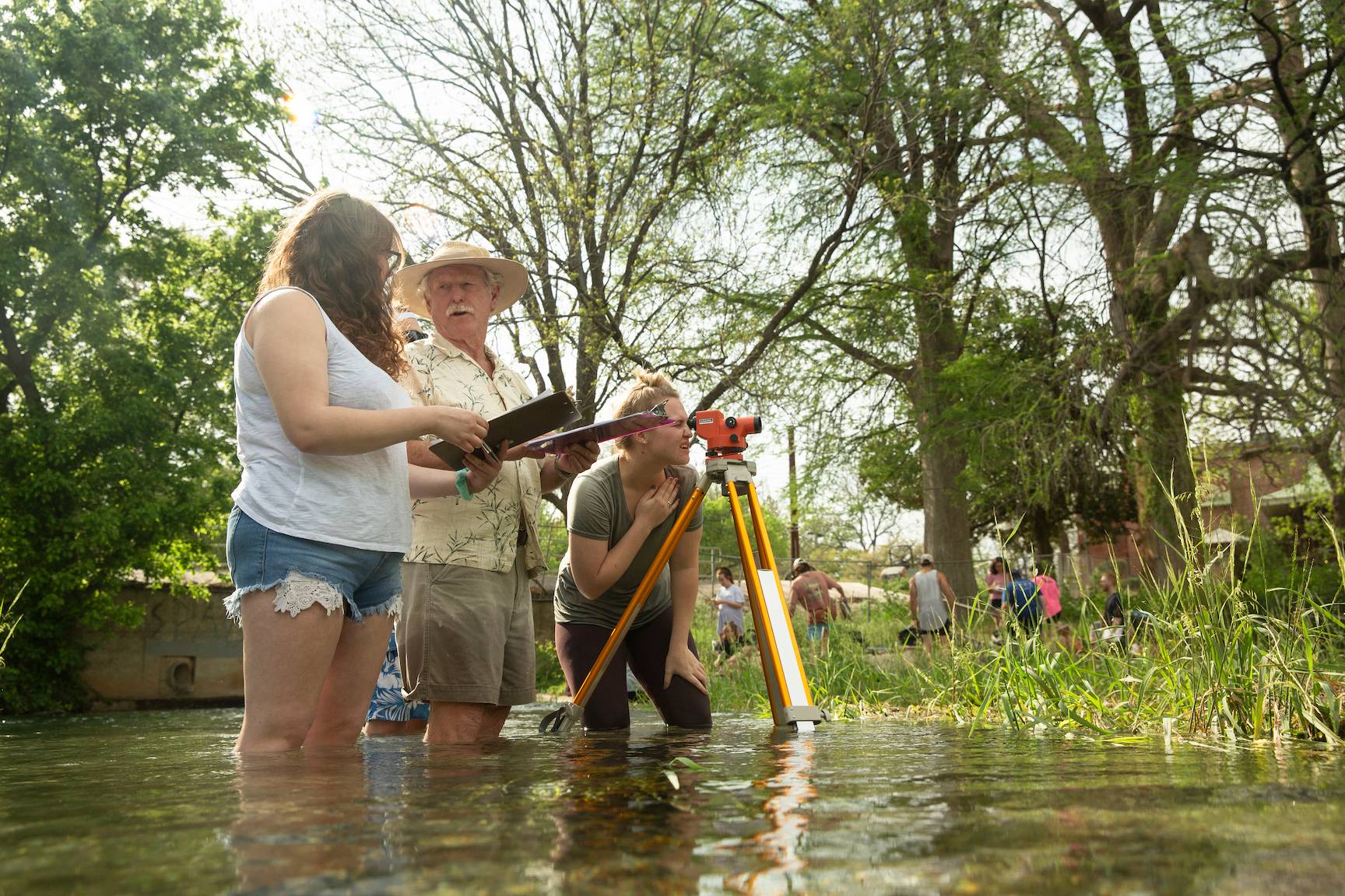 Students and faculty standing in knee high water doing a survey with a geographic tools