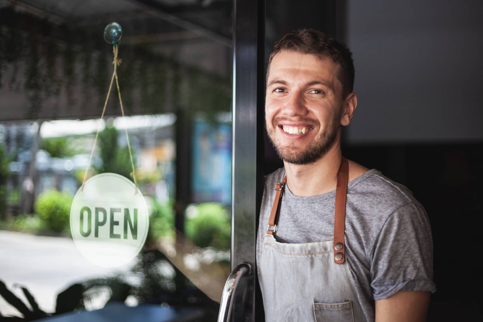 Man holding a cafe door open with a sign on it that reads "Open"