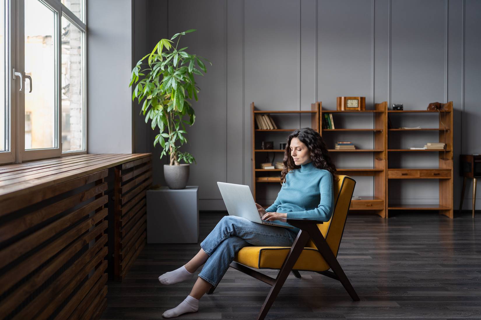 Person sitting in a chair near a window. A laptop rests on their lap