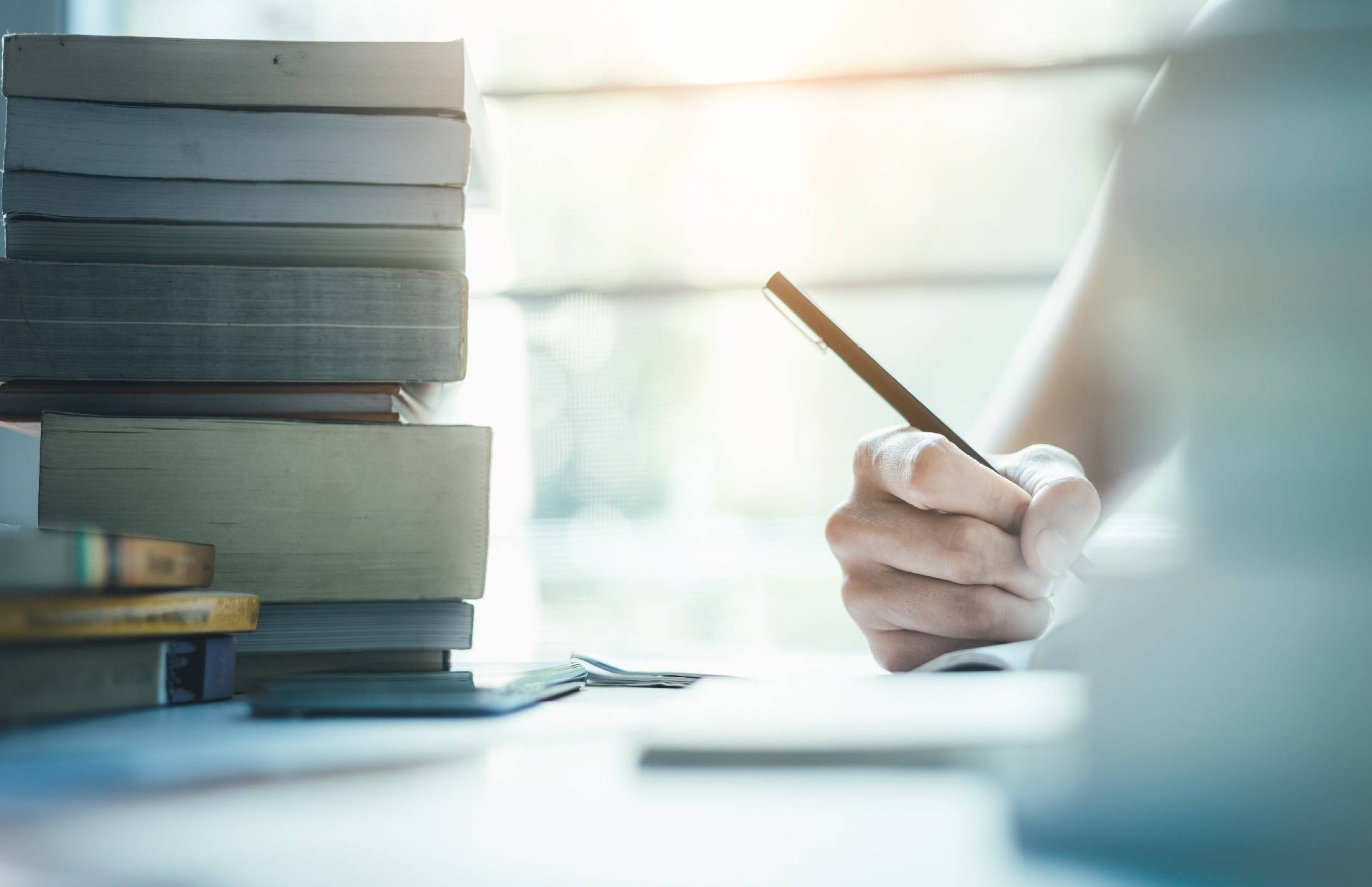 Person writing in a notebook with books next to them.