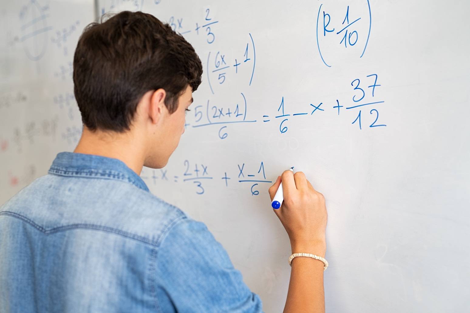 Young man writing math equations on a white board