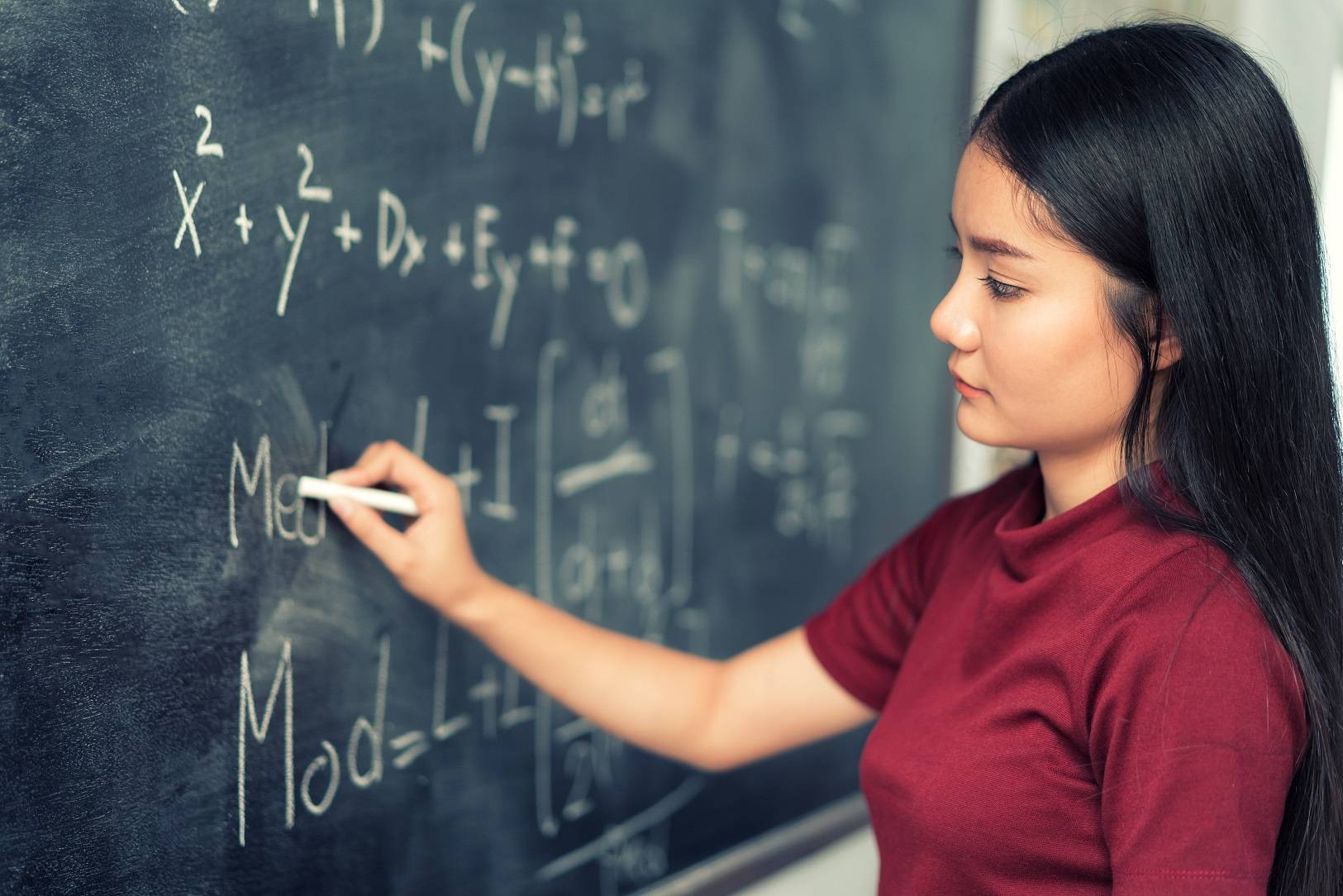 Young woman writing math equations on a chalk board.