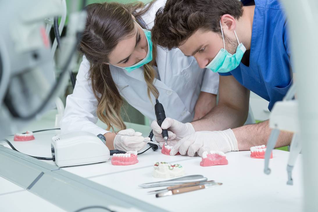 2 dental students practicing on model teeth