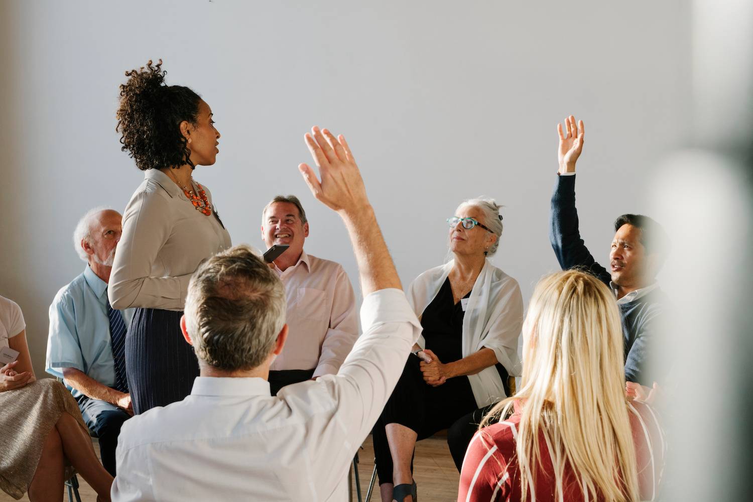 group of people seated around a standing instructor. Two of them have their hand raised.