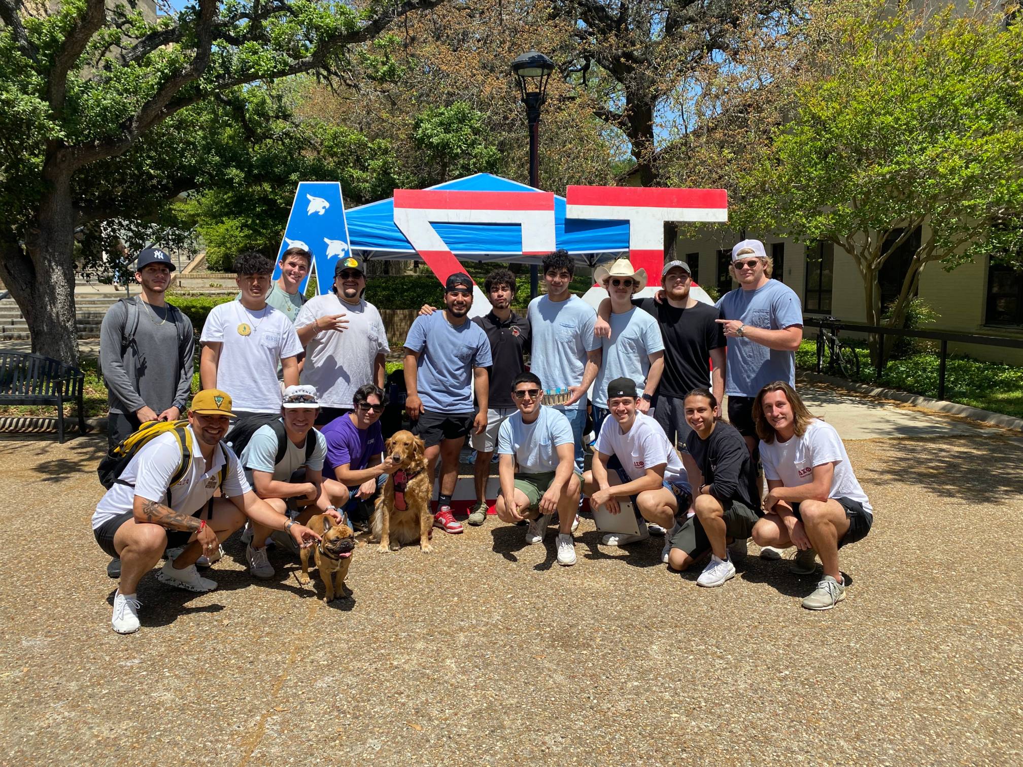 Men of Delta Sigma Phi pose in the Quad in front of their letters. Two dogs are also in the photo.