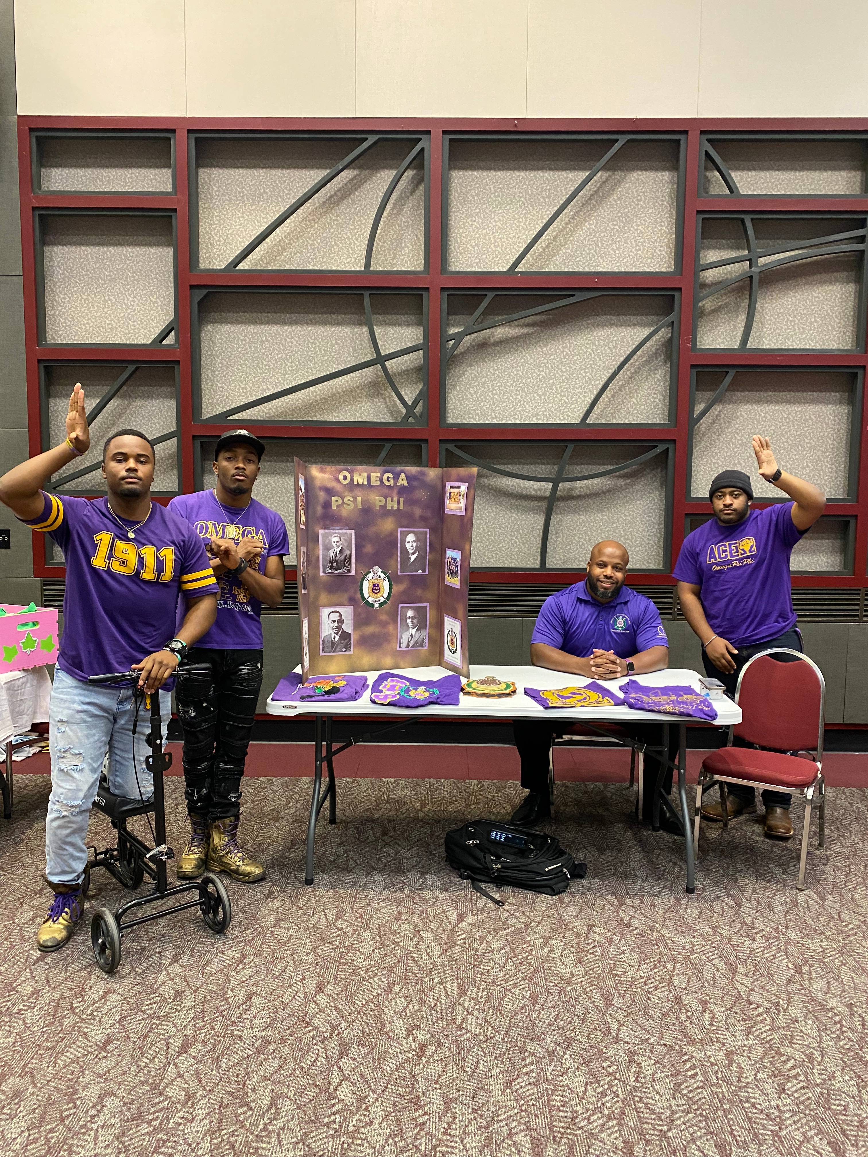 Men of Omega Psi Phi wearing their organization's colors and showing their hand signs while tabling in the LBJ Student Center Ballroom