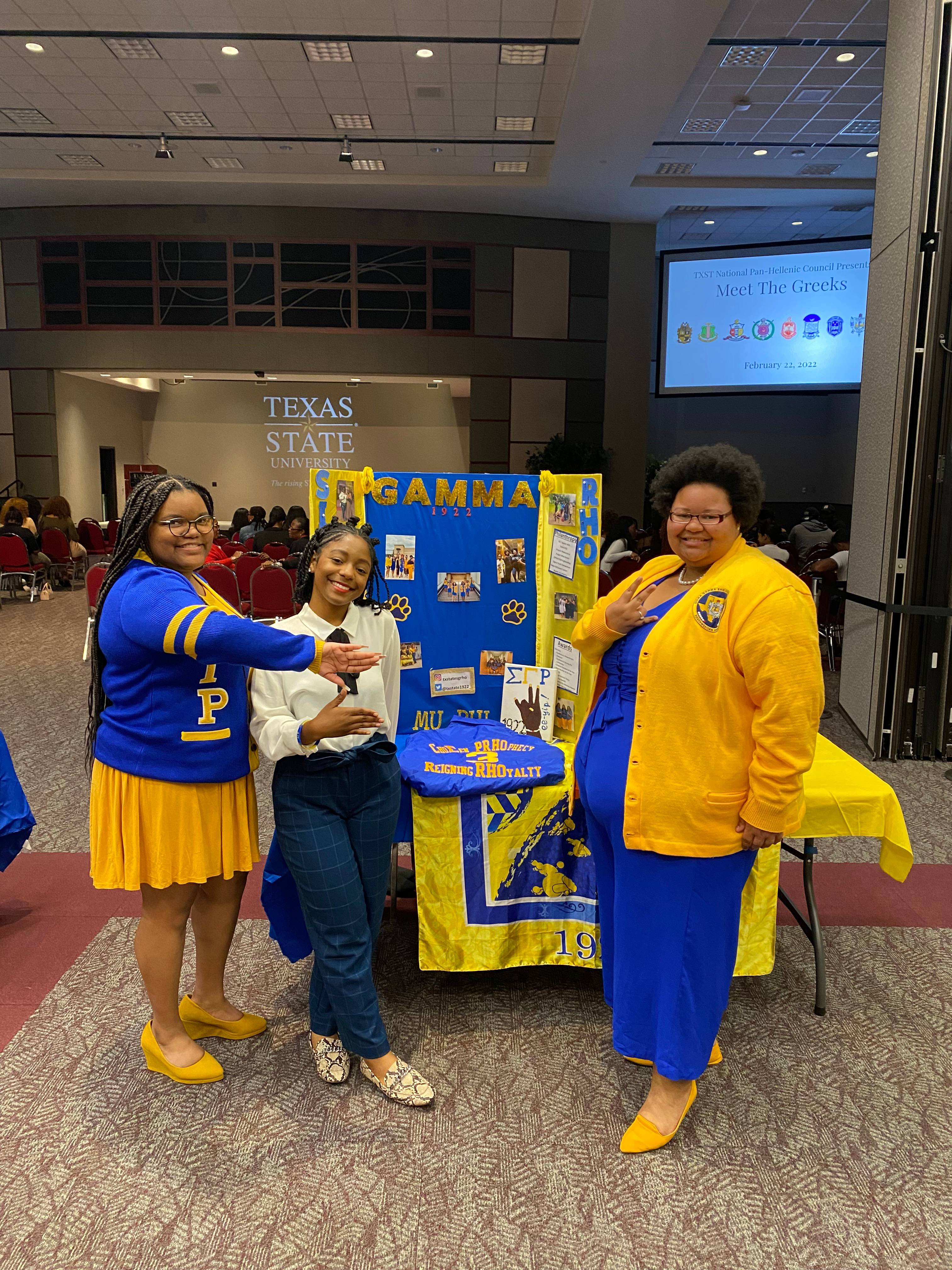 Women of Sigma Gamma Rho wearing their organizations' colors and showing their hand signs while tabling in the LBJ Student Center Ballroom