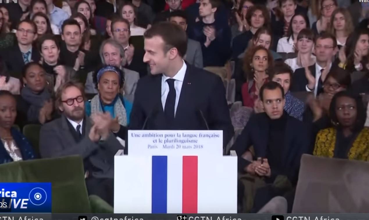 Man speaking at podium with French flag in front of audience