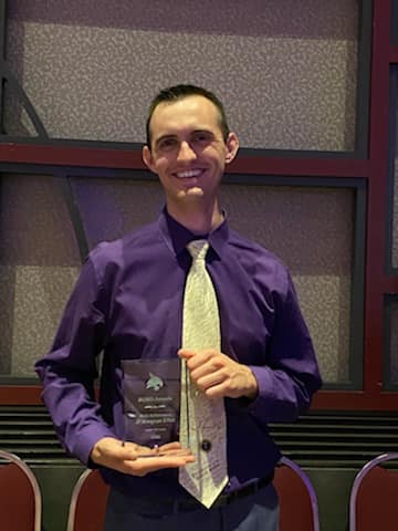 man wearing purple shirt and light tie holding award
