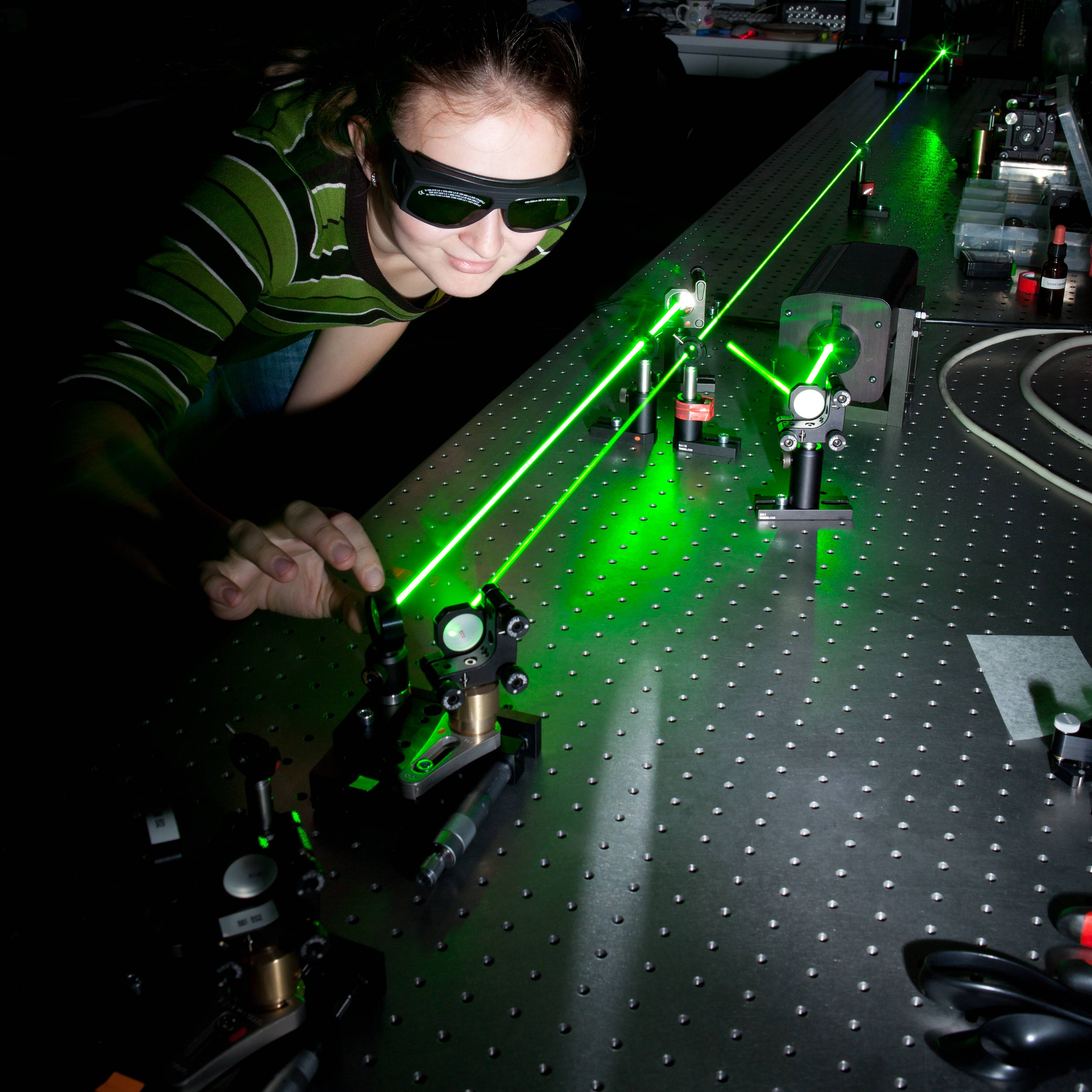 girl looking at green laser beam in quantum physics laboratory