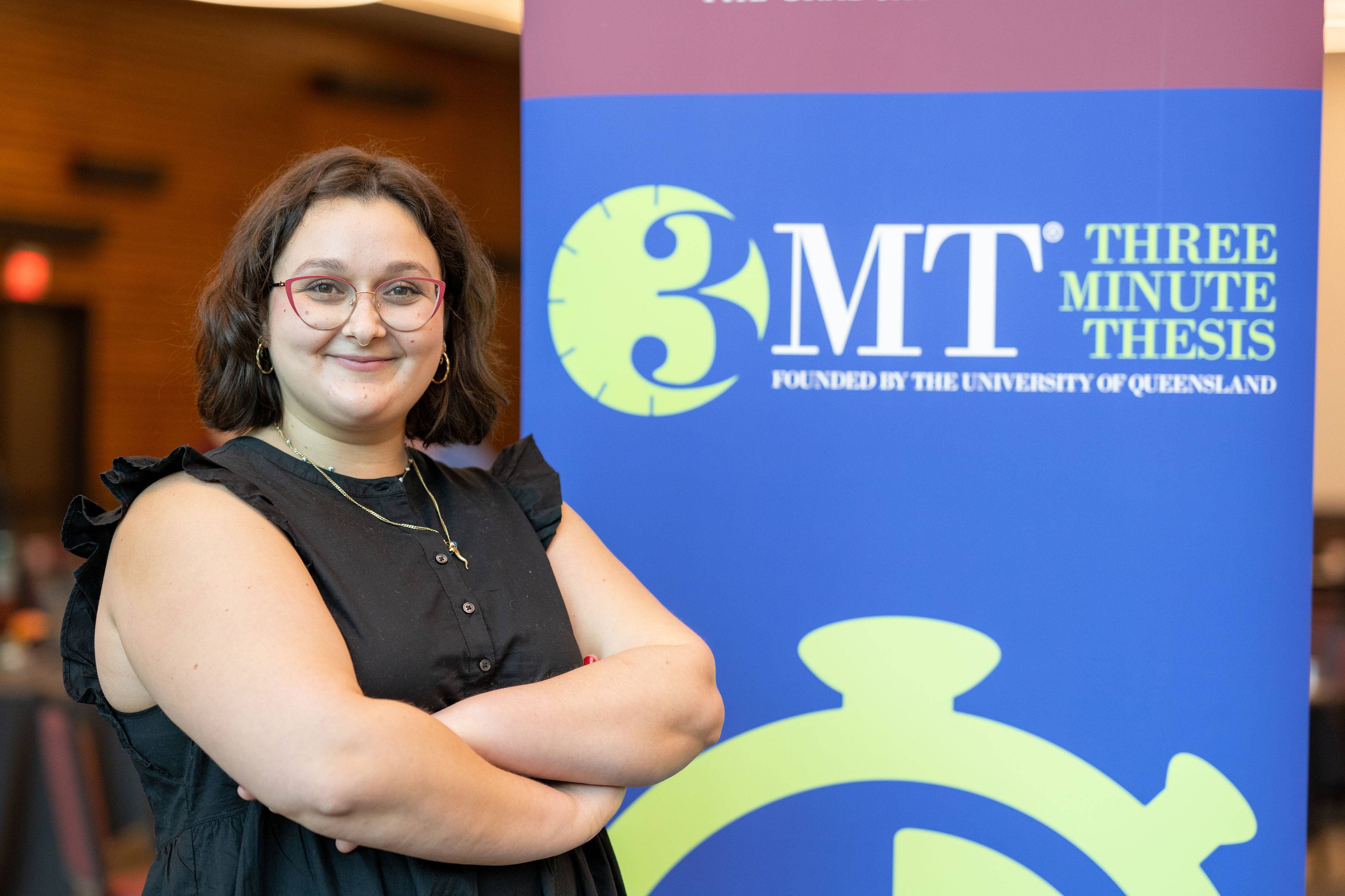Kayra Tasci standing next to a 3MT sign with her arms crossed