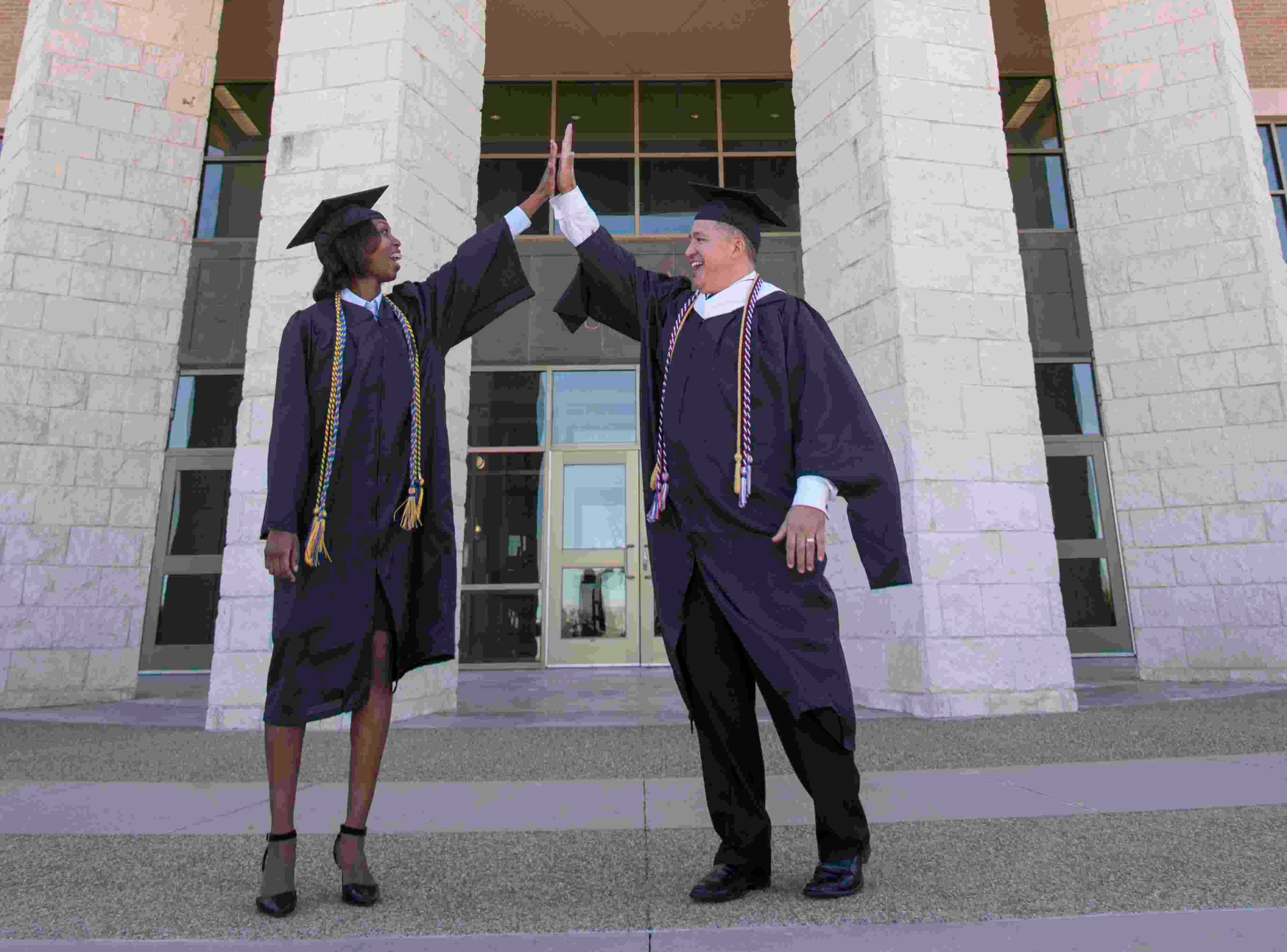 two students in commencement attire give a high-five