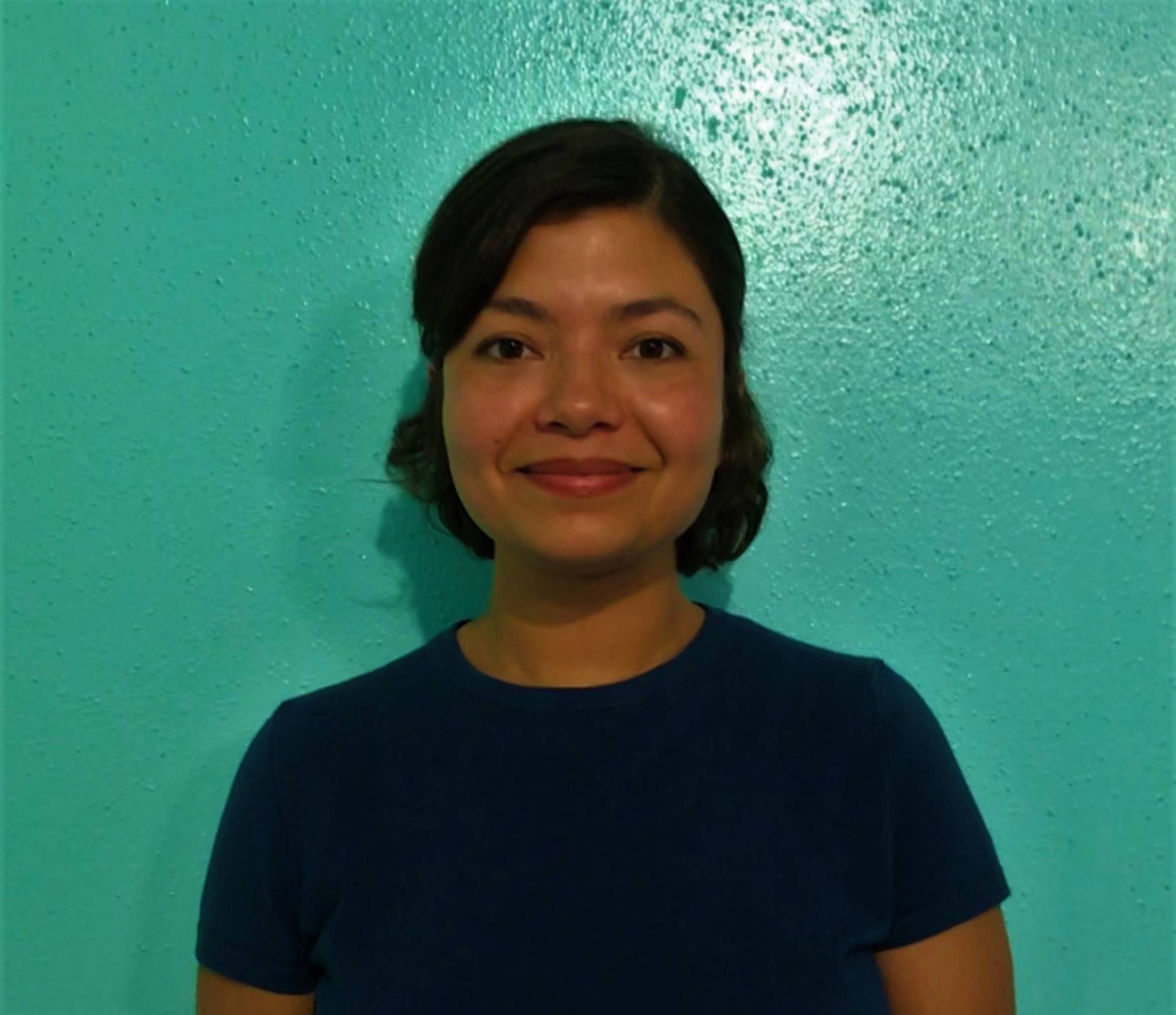 Laura Vazquez Arreguin stands smiling in front of a teal-colored wall