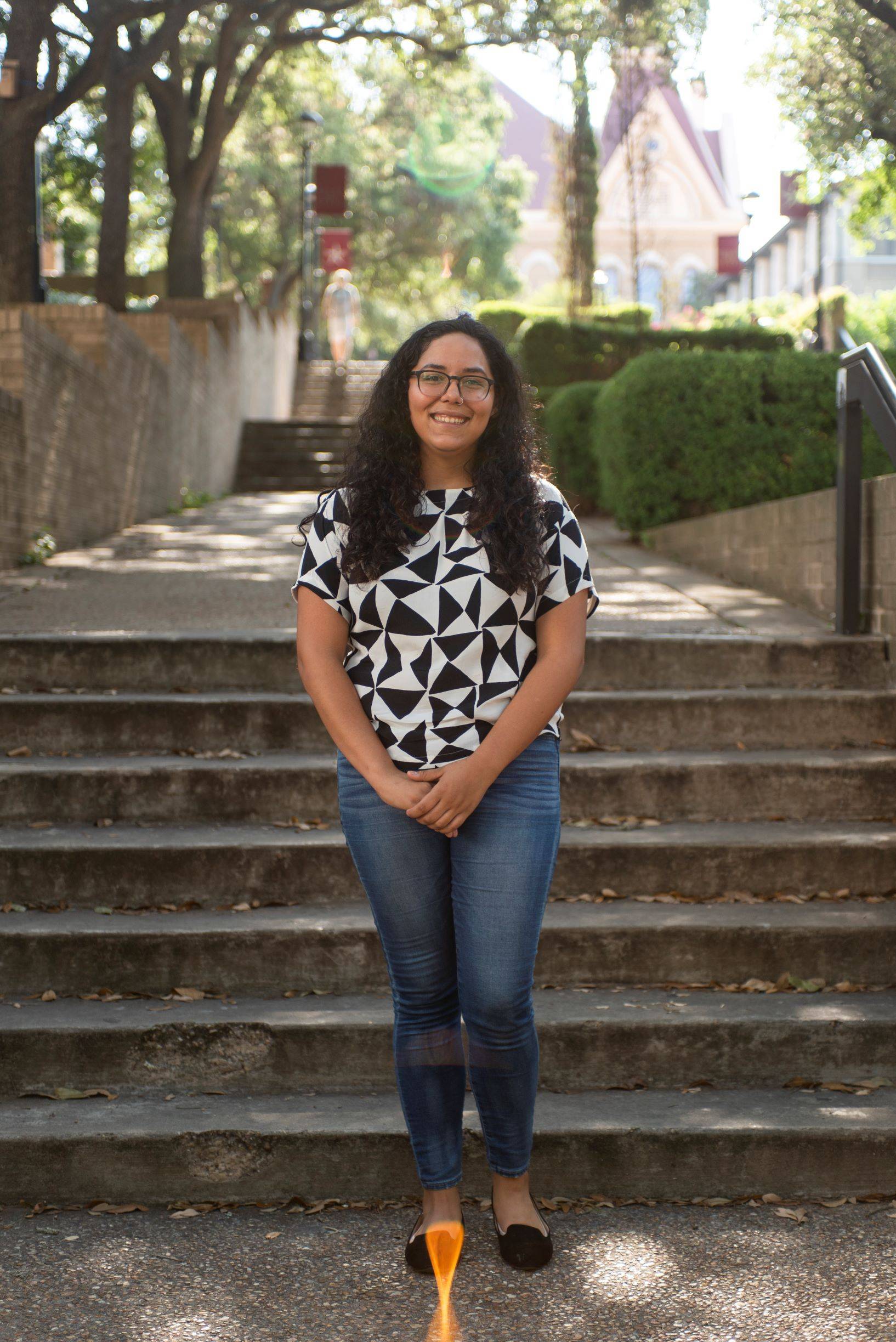 Elisia Paiz stands in front of the steps leading up to Old Main. She is smiling and holding her hands in front of herself.