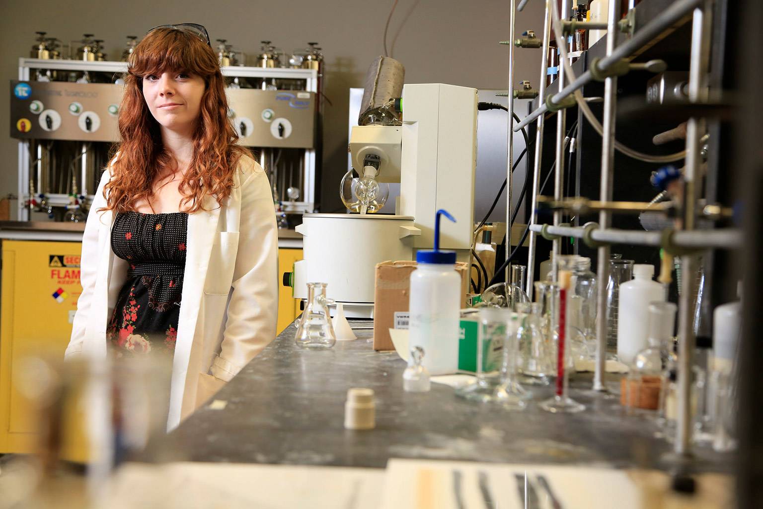 a female student in a white coat looks at the camera in her lab