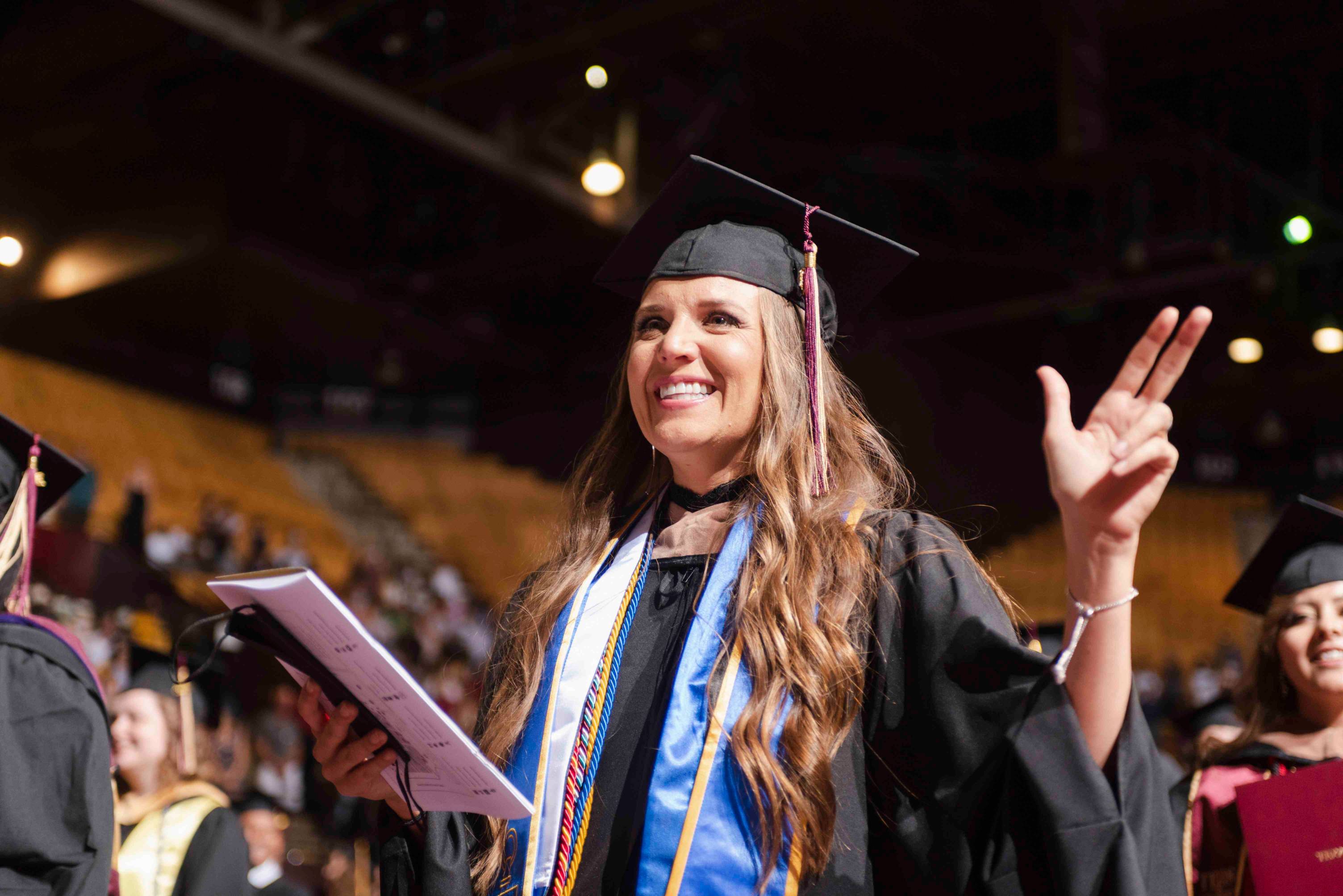 a woman at commencement smiles and makes the texas state hand sign