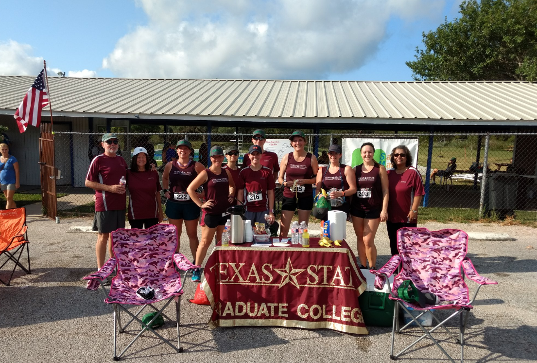 Group of runners standing behind the Texas State Graduate College table