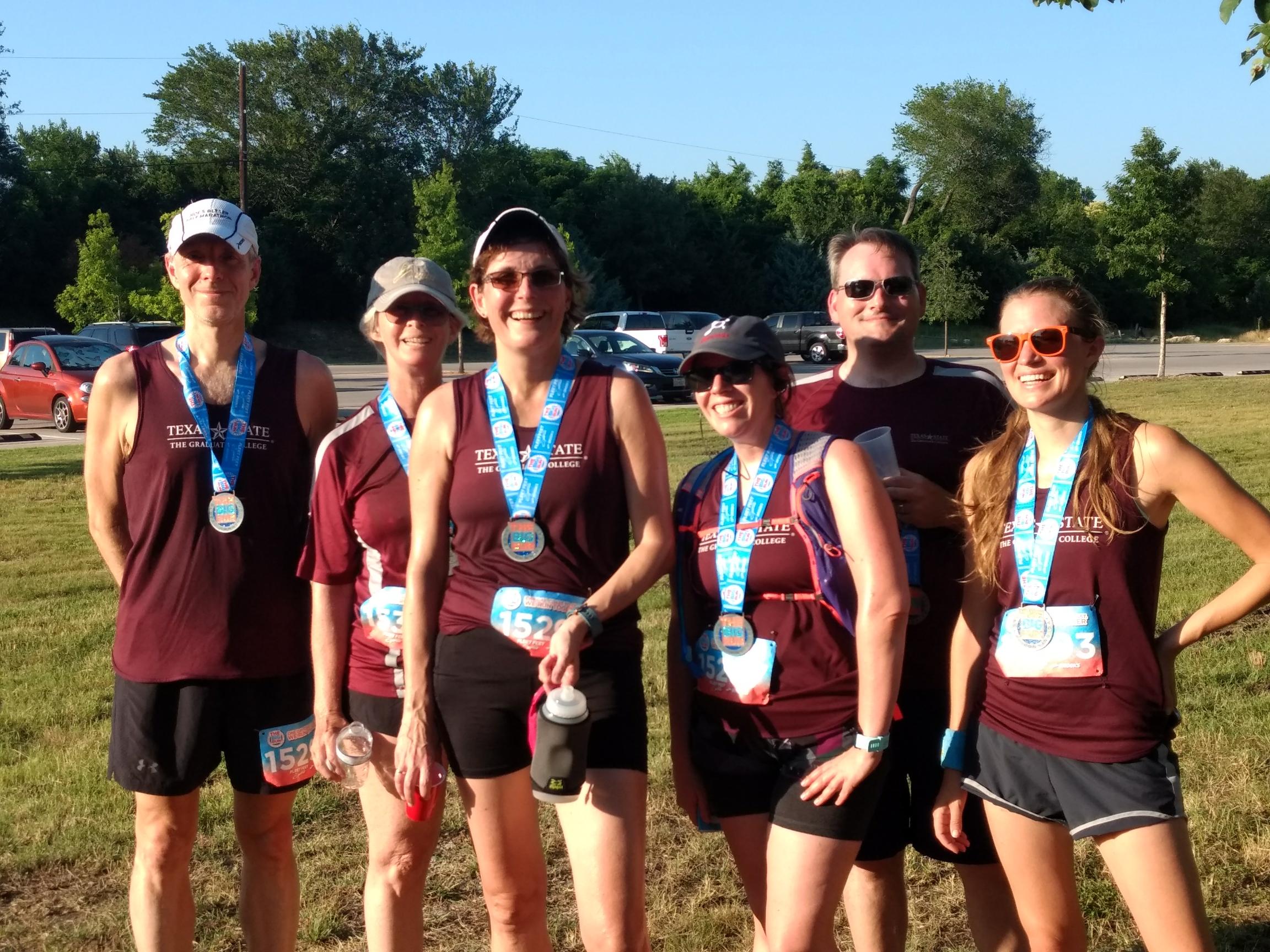 six runners in the maroon "Running With the Grad Deans" shirt take a photo after The Big Run race