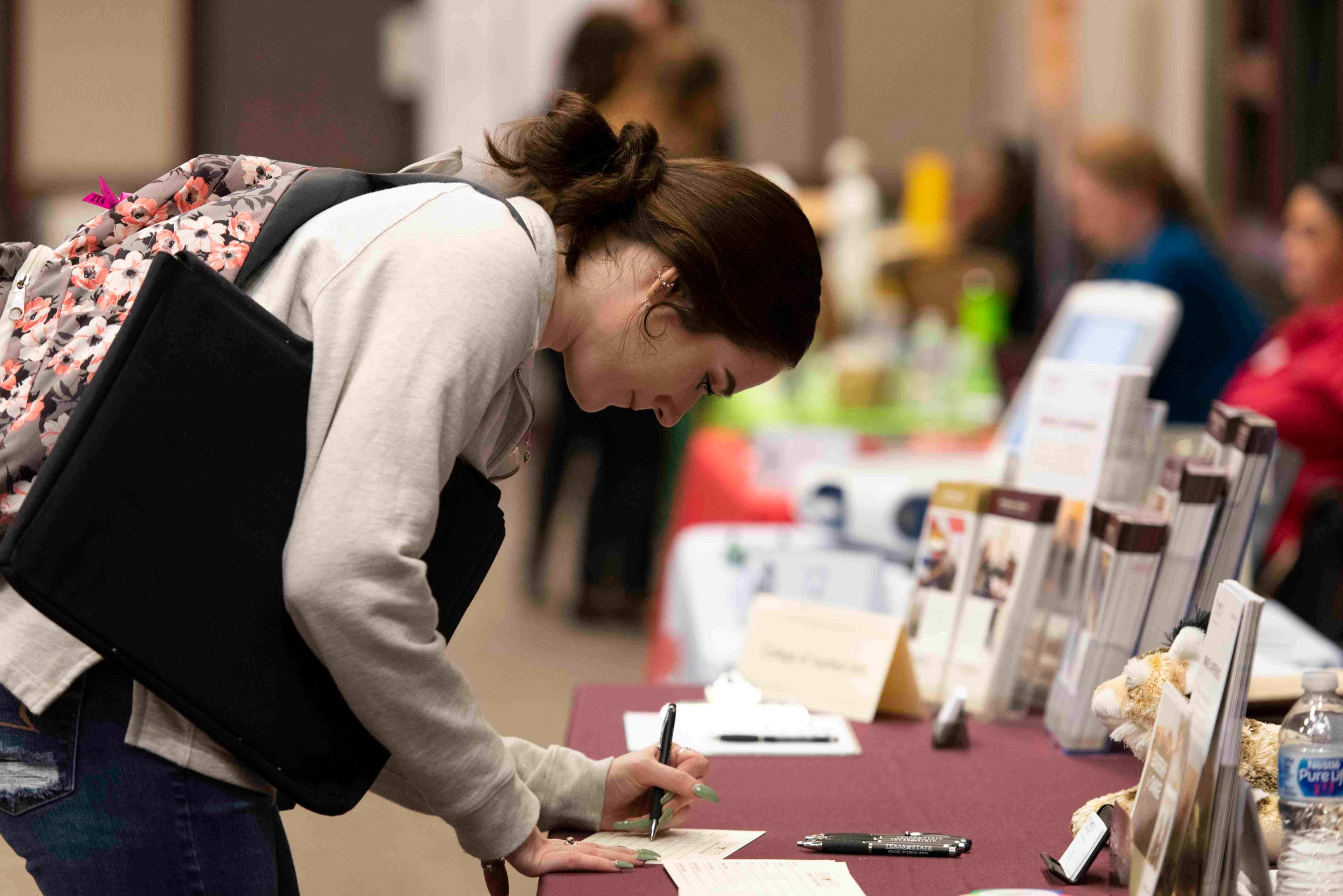 a female student fills out a request info card at a booth during a fair
