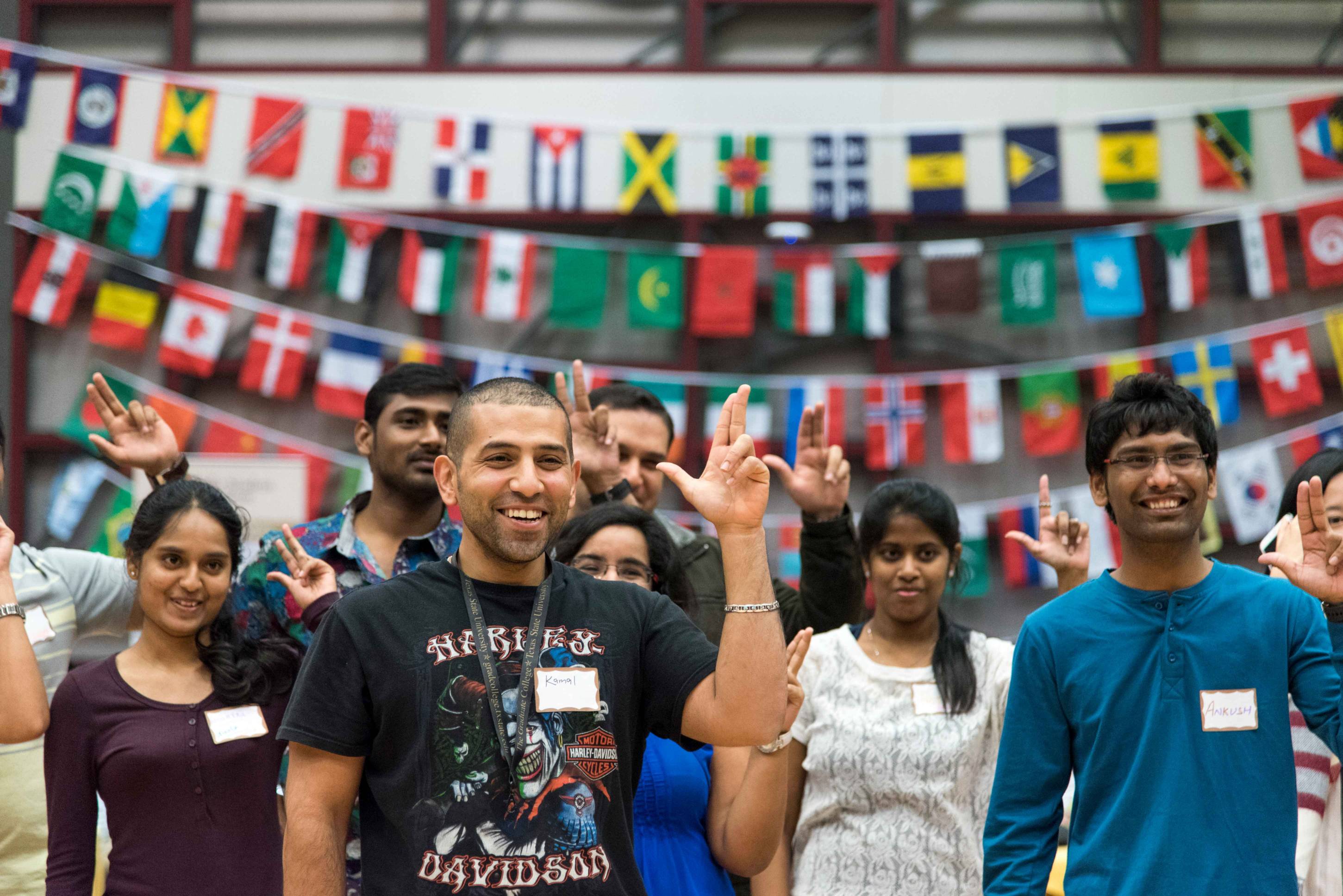 a group of international students make the texas state hand signs in front of a banner of various country flags