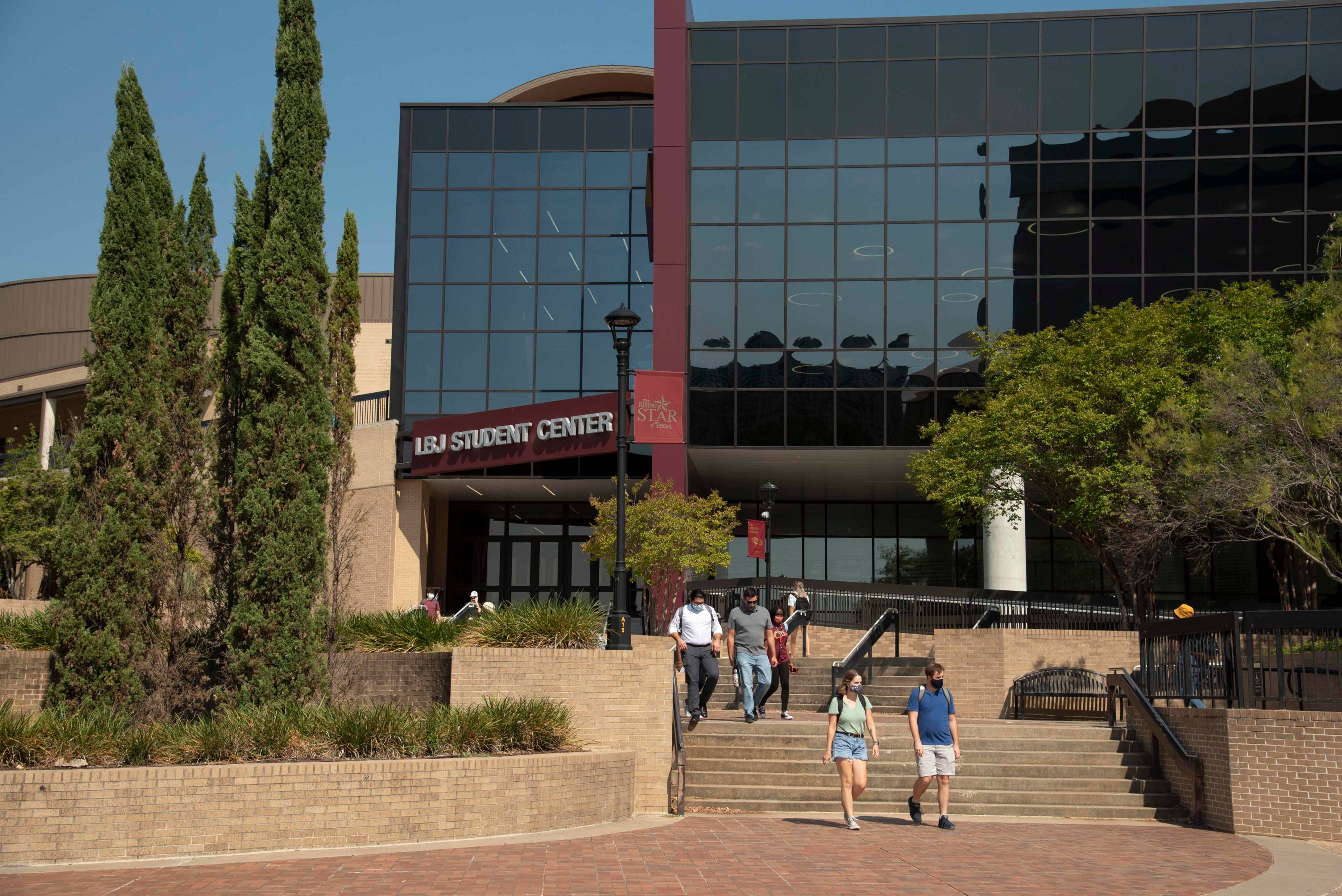 the front exterior of the LBJ student center with several students walking up and down the steps