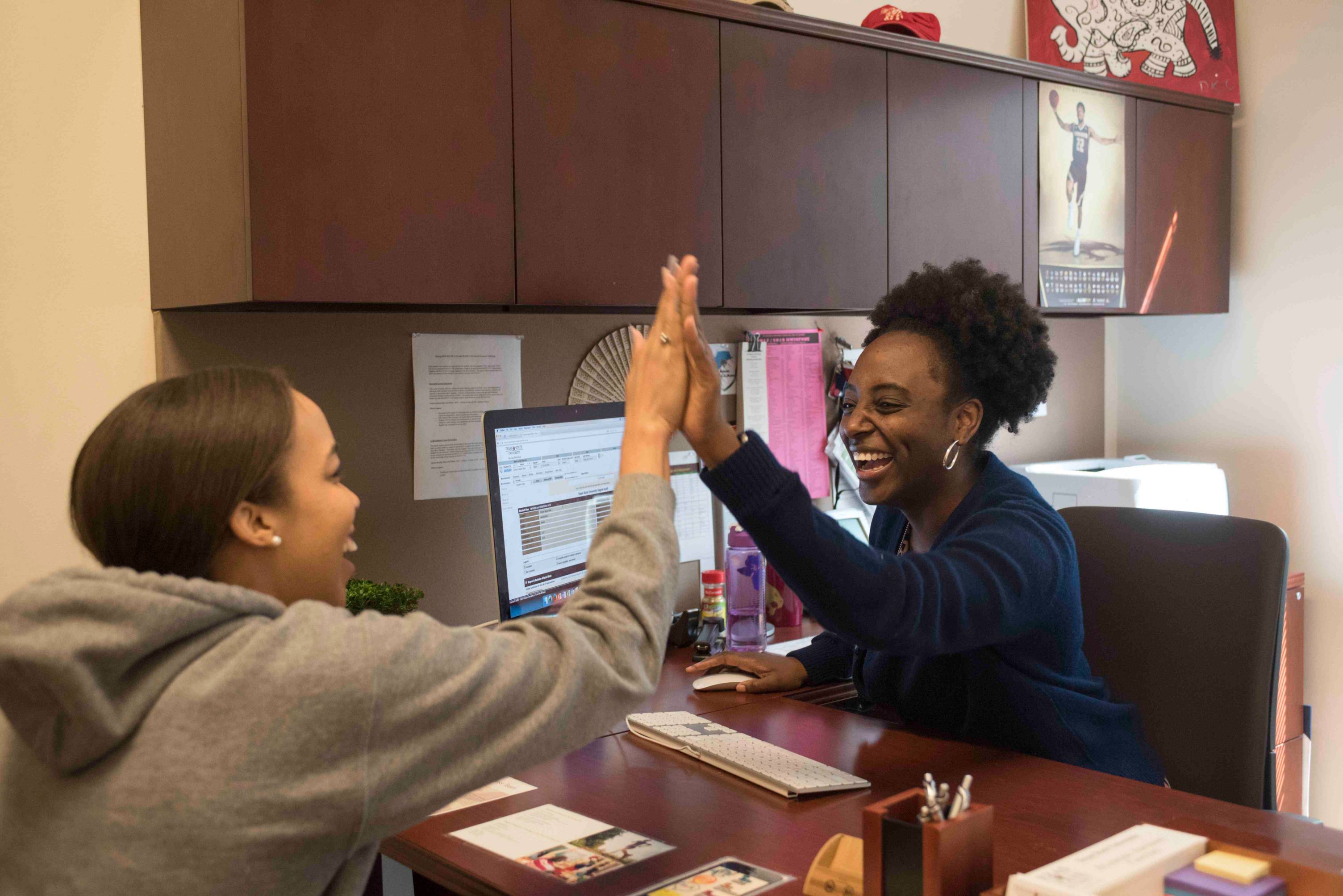 a graduate advisor gives a student a high five in her office