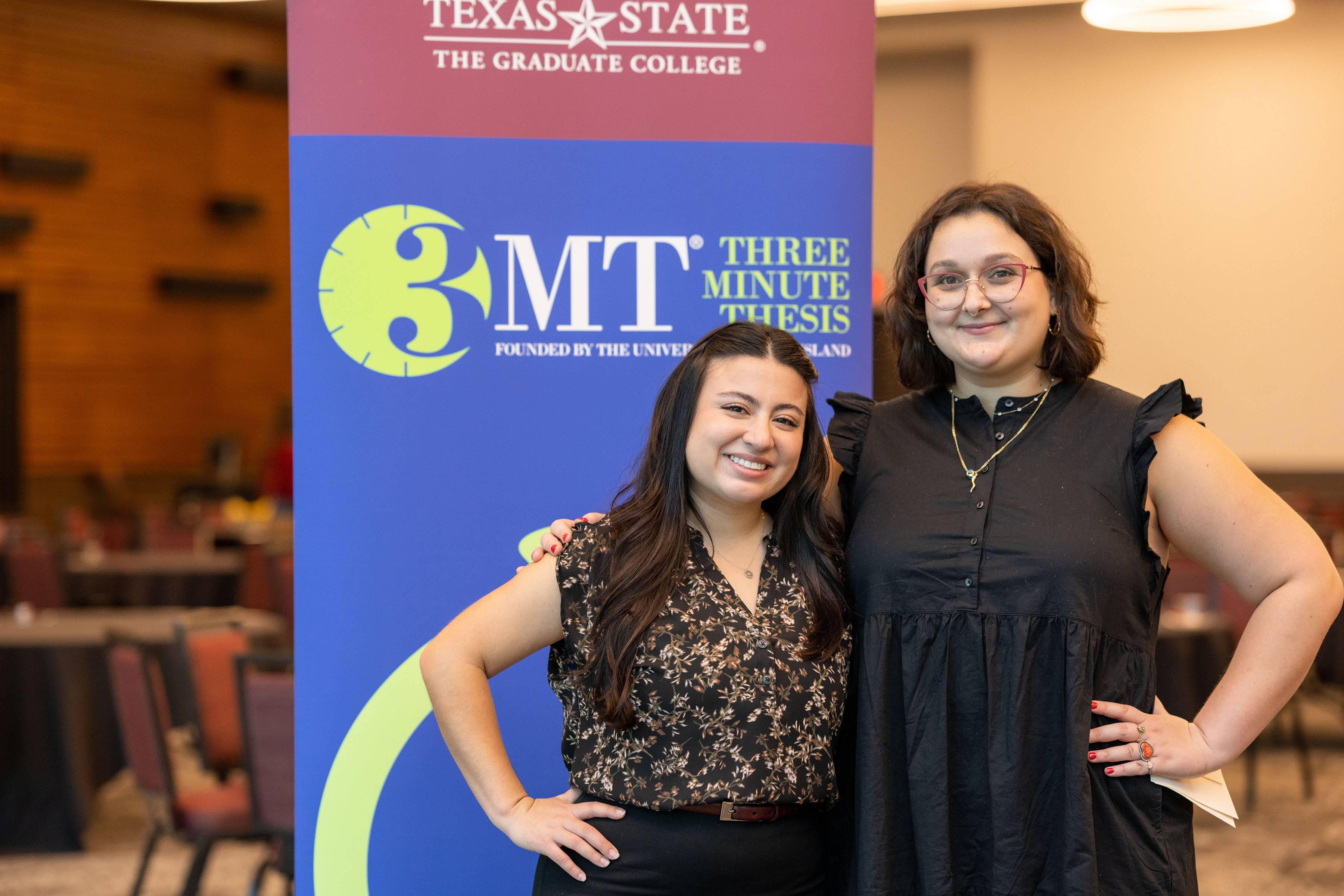 Brianna Fogel (left) and Kayra Tasci (right) pose in front of a Three Minute Thesis sign at the Three Minute Thesis University Final