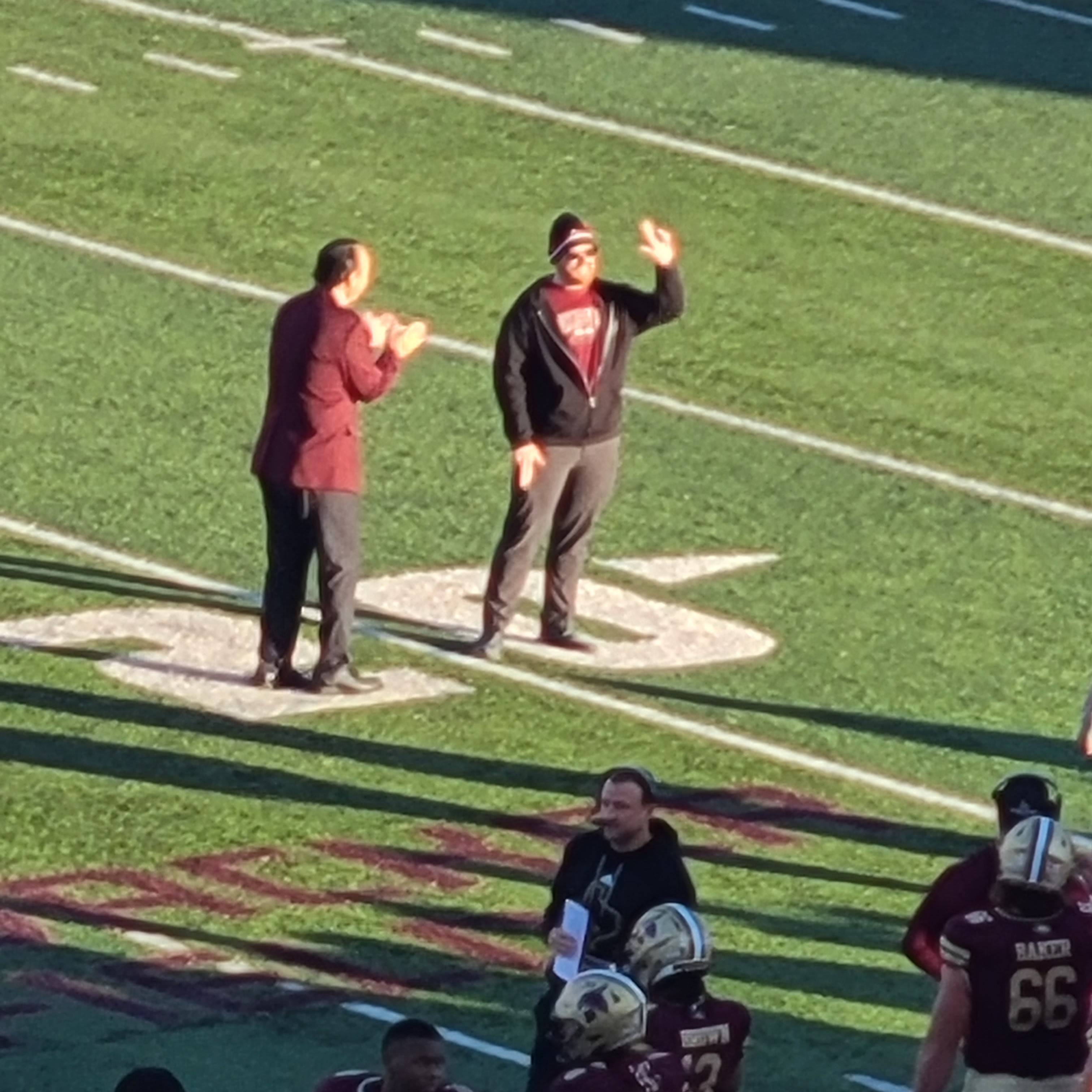 Mark Moore on the football feild with President Damphouse holding up the TXST hand sign with his left hand