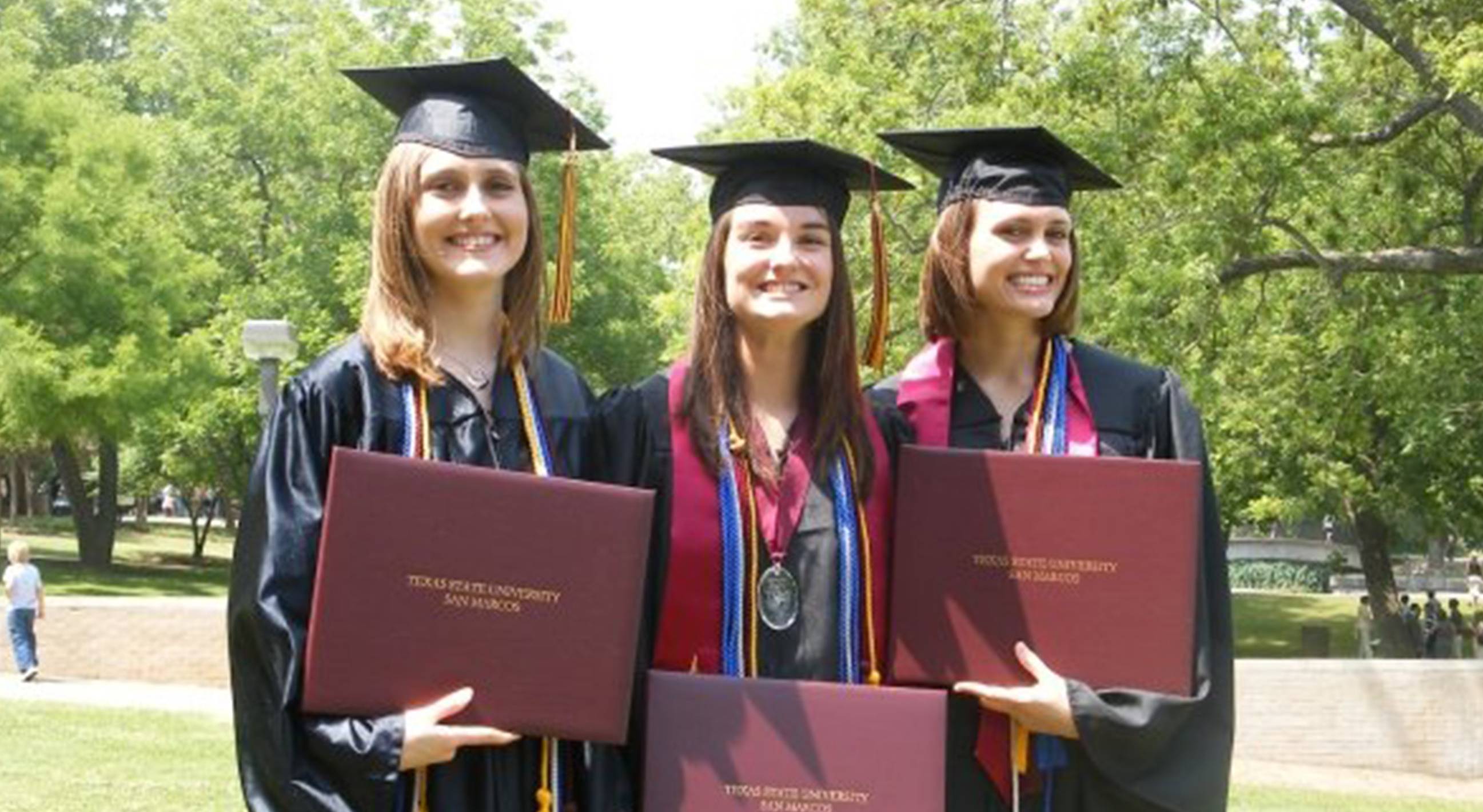 three graduates smiling with diplomas