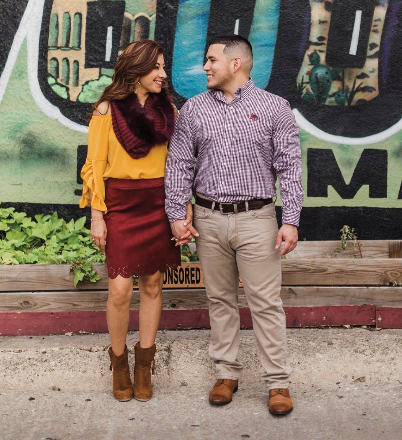 young couple smiling in front of mural