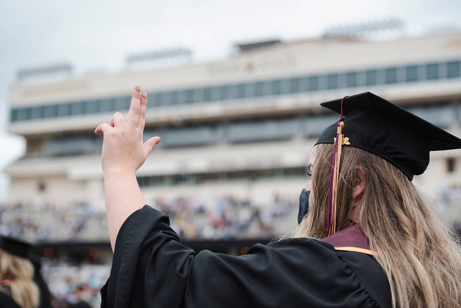 female graduate holding up txst hand sign