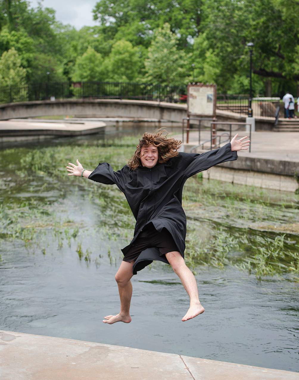 woman in graduation gown jumping into river