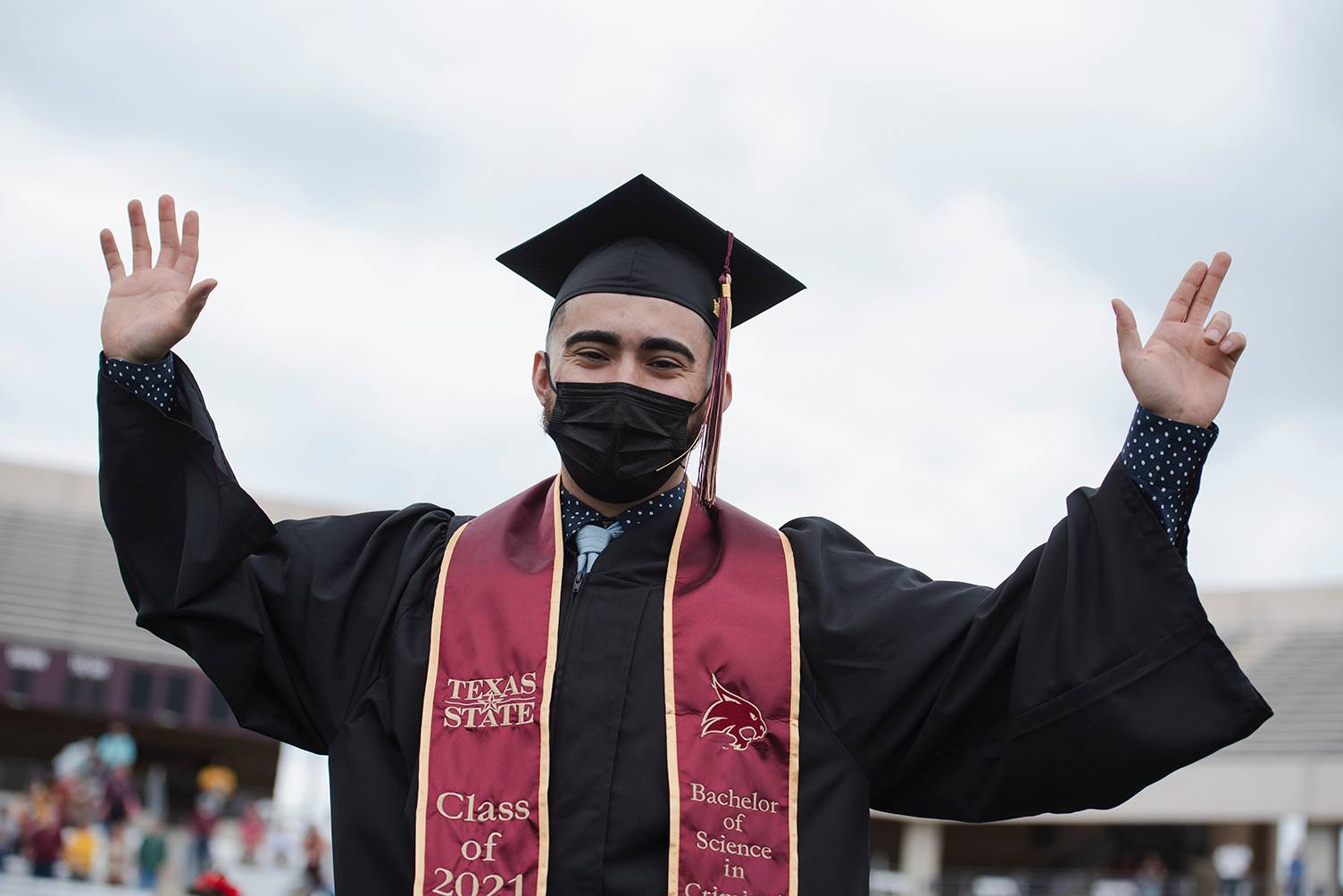 male graduate holding up txst hand signs