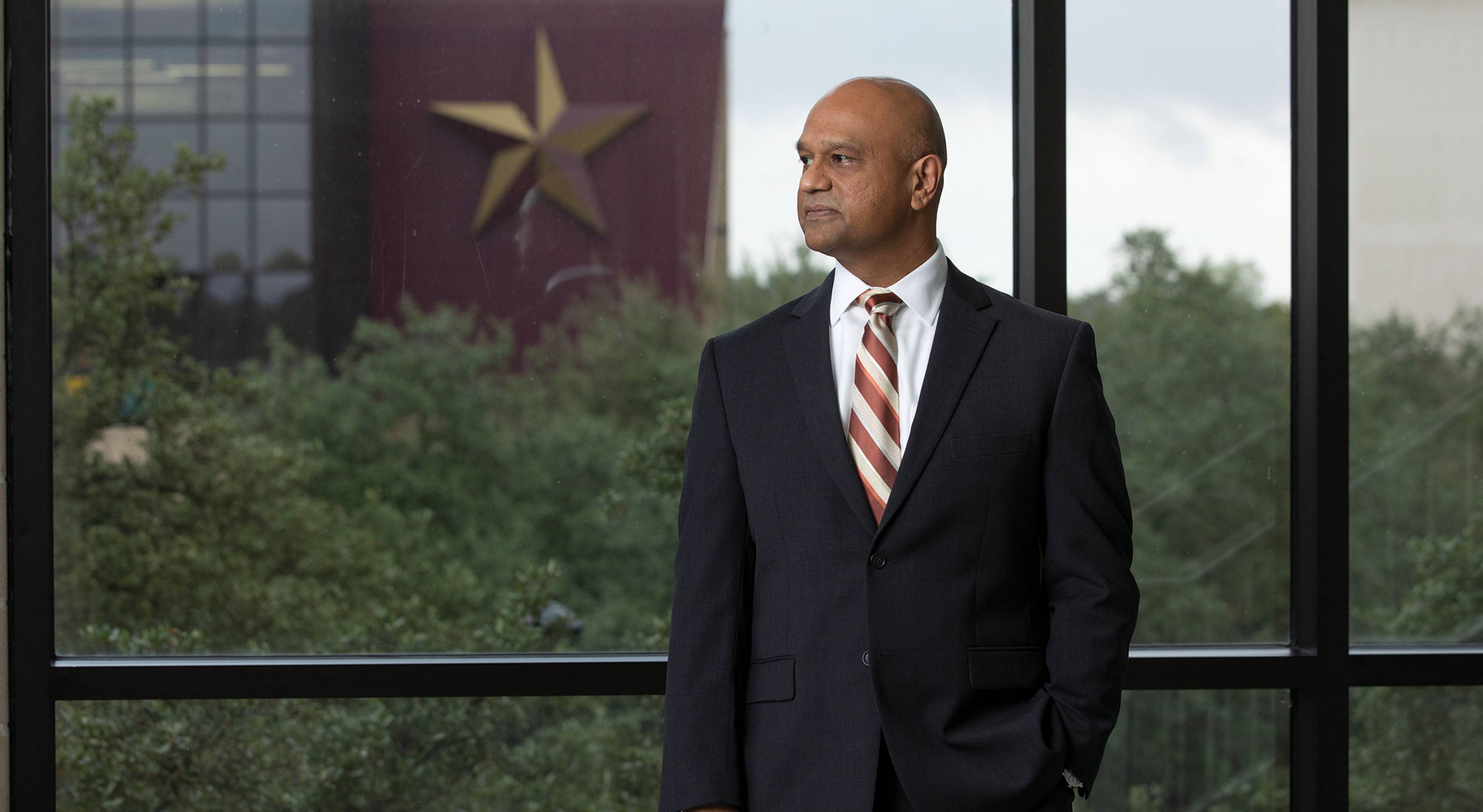 man in professional clothing standing in front of window with building in background