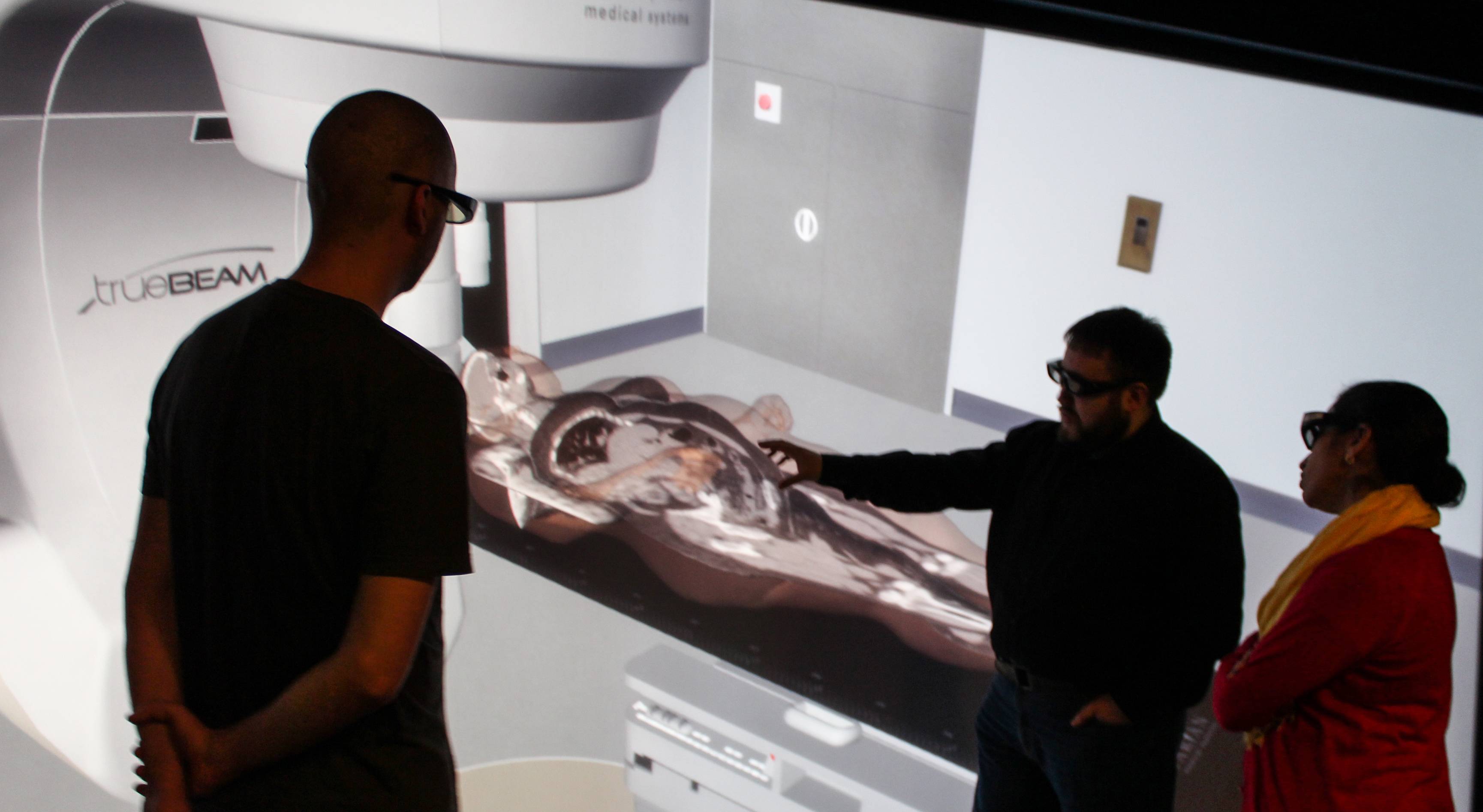 three people looking at 3d model of body in radiation machine