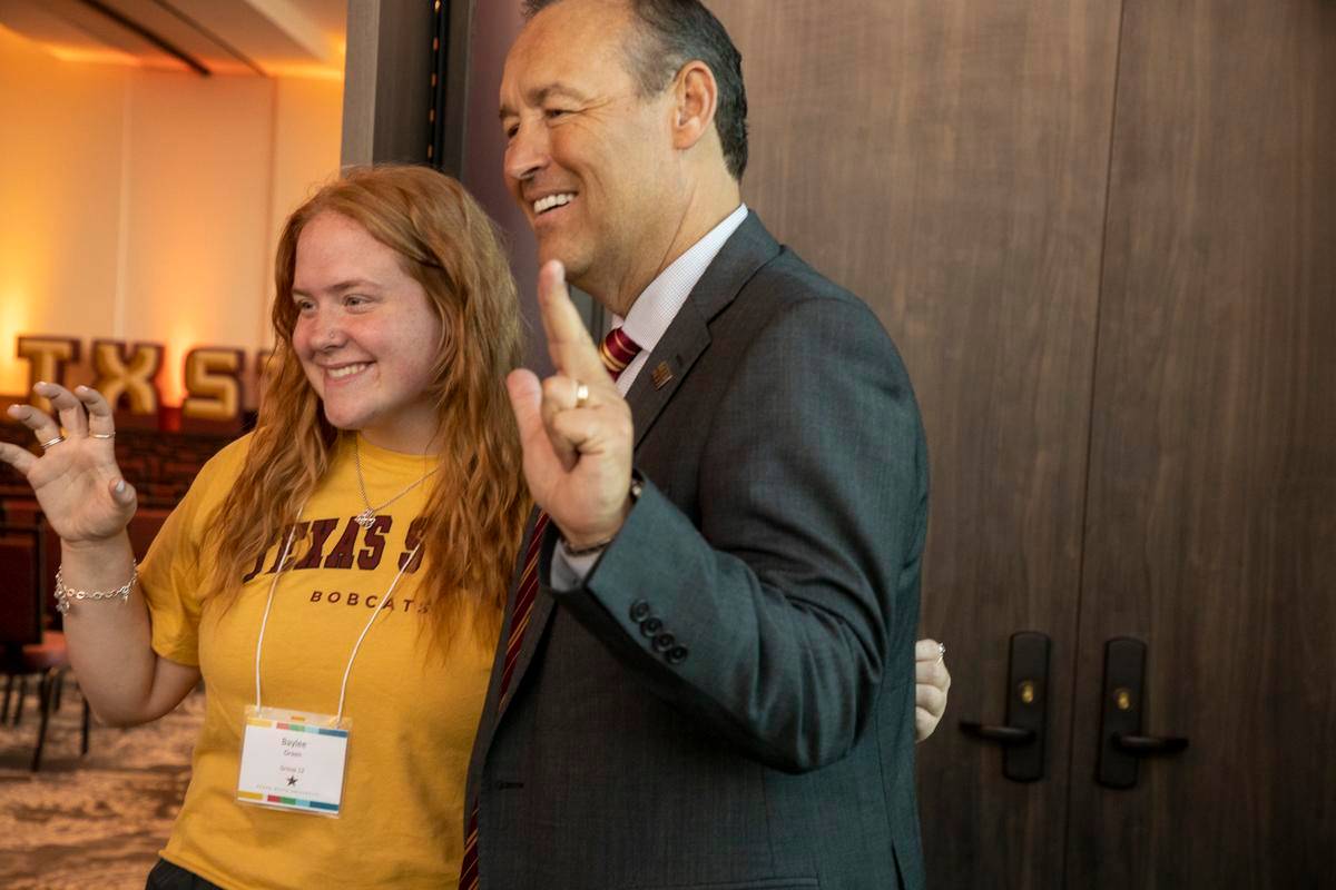 kelly damphousse and young woman doing the txst hand signs