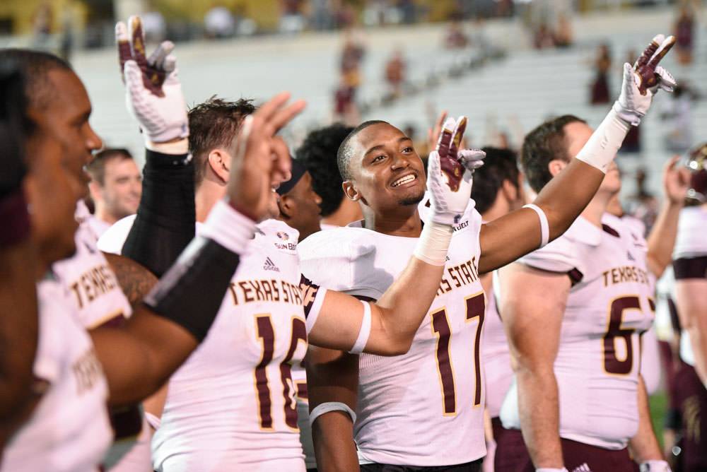 football players wearing Bobcats jerseys while waving the txst hand sign in the air