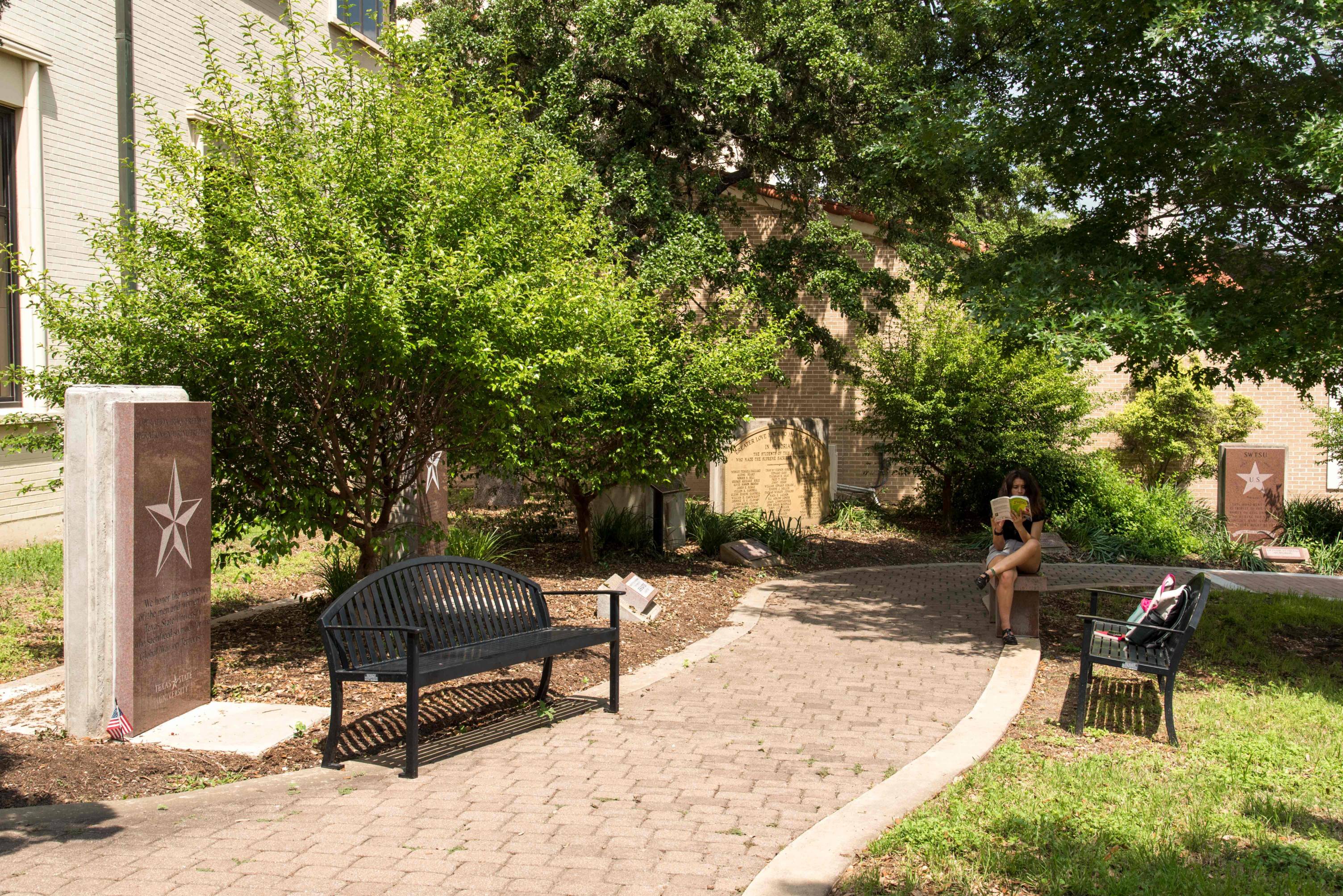 a walkway surrounded by greenery and has three stone memorial plaques