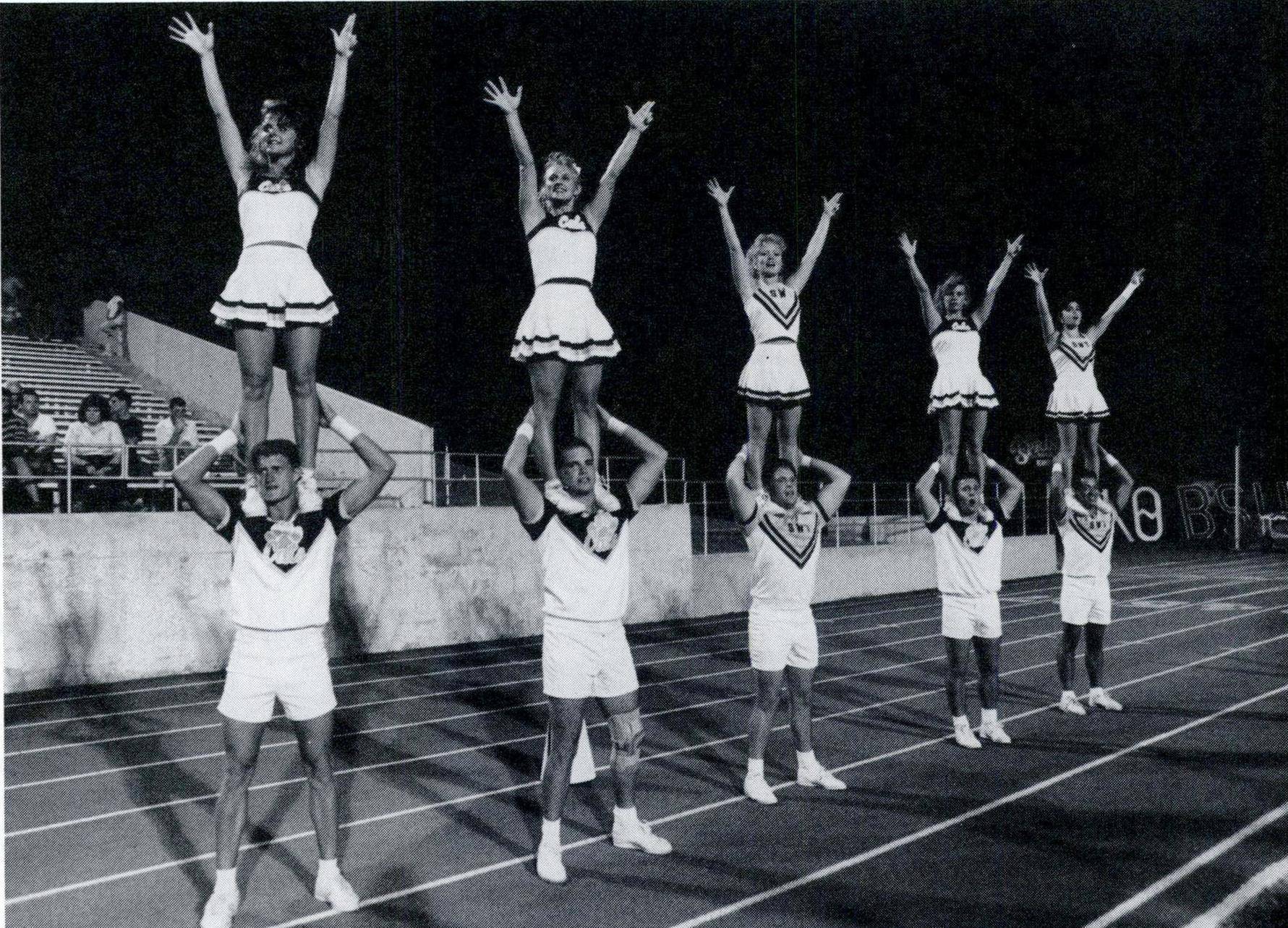 black and white photo of female cheerleaders holding up the txst hand signs while standing on male cheerleaders' shoulders