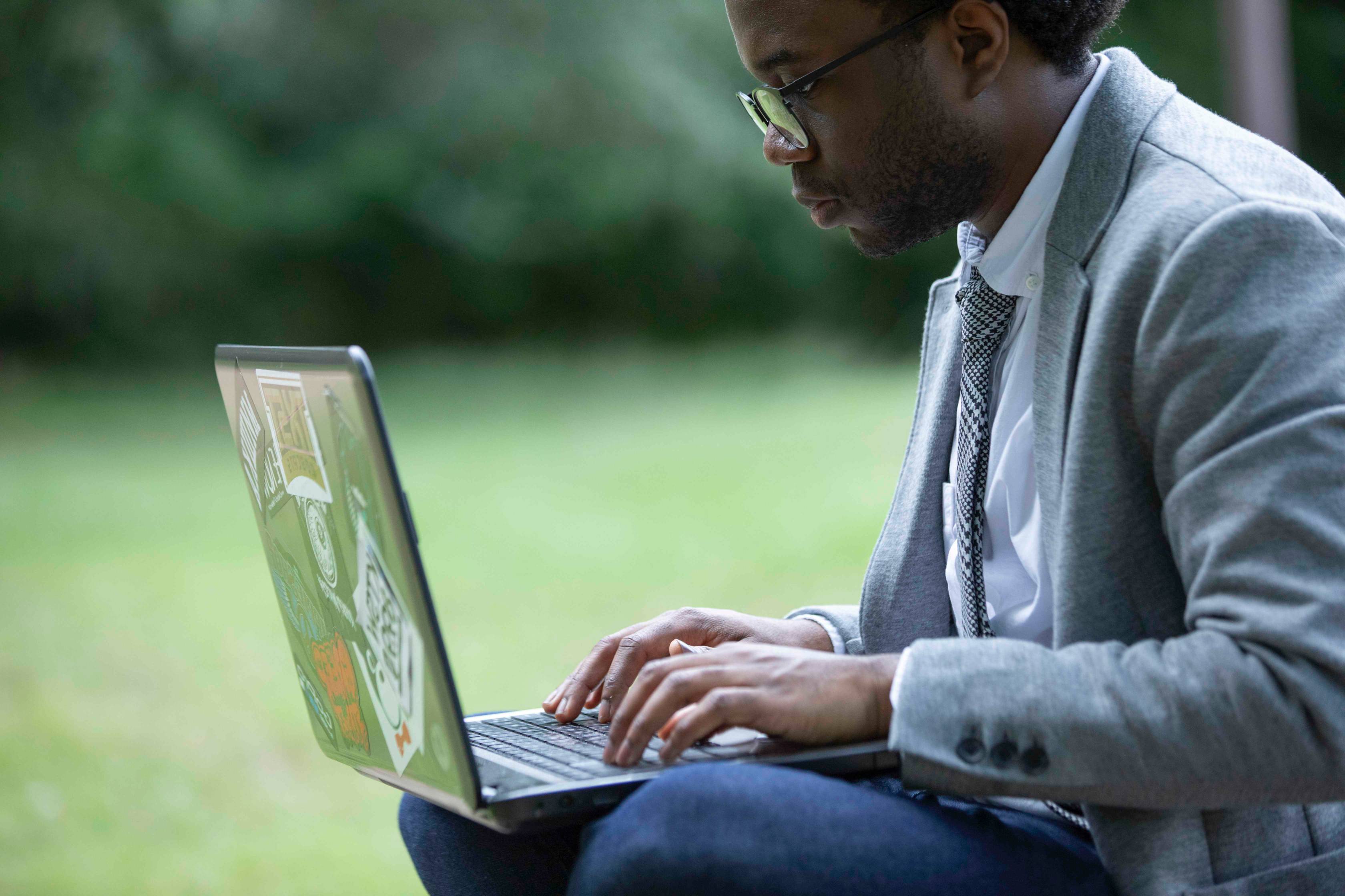 a black male student sits outside with his laptop in his lap