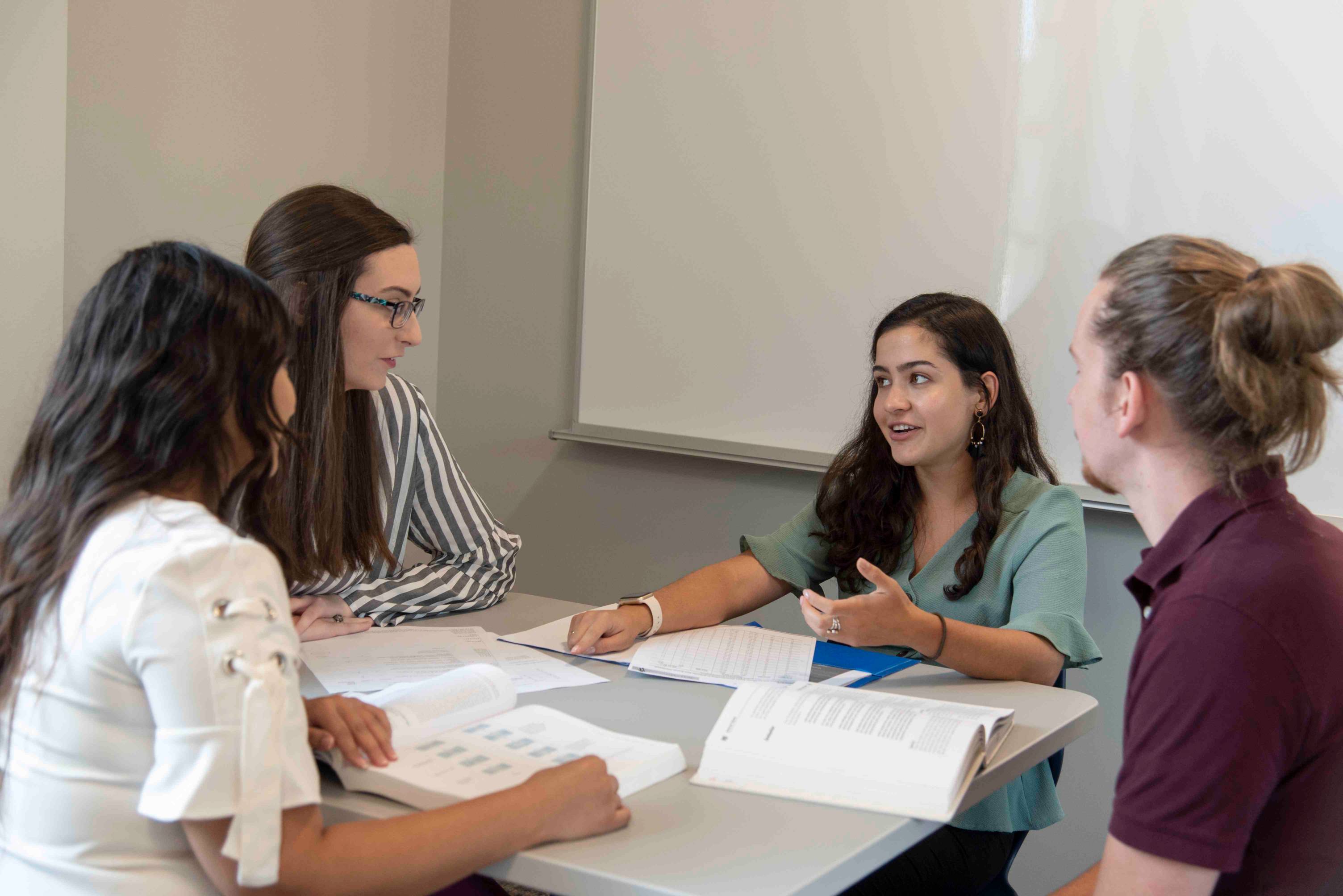 a group of four students sit at a study table table and discuss with open books in front of them