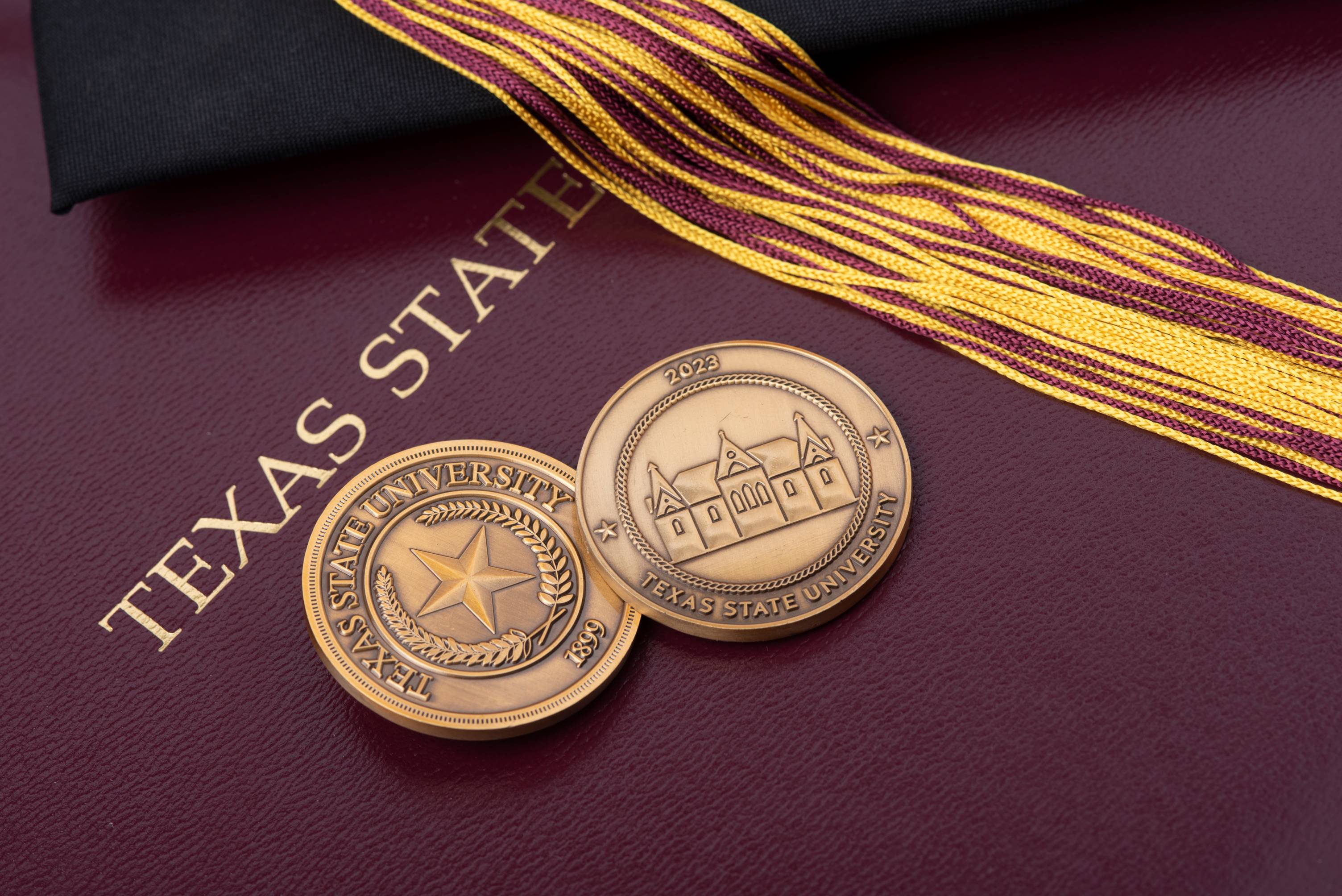 Texas State University challenge coins front and back on maroon diploma board