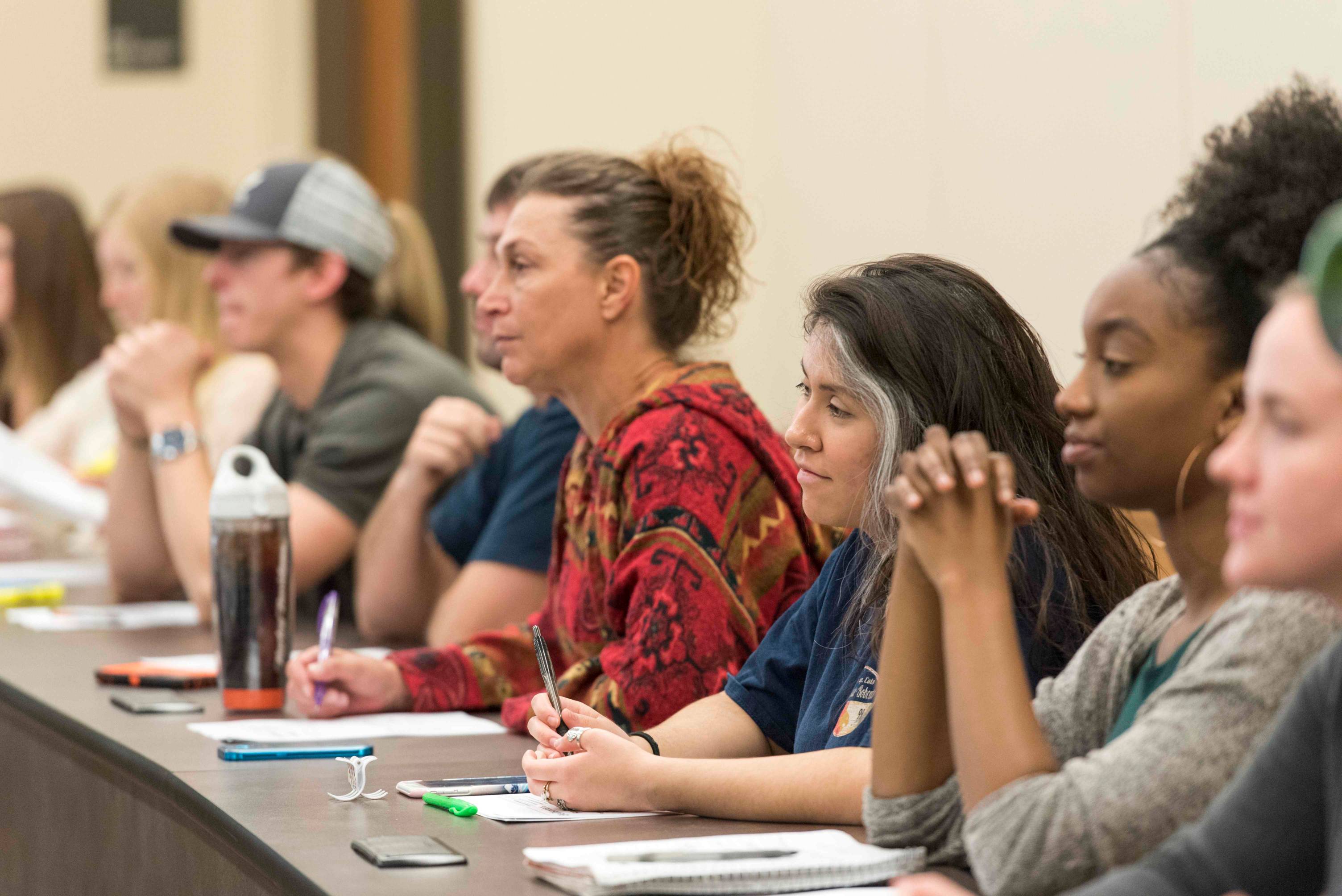 a group of students sit at a long desk while listening to a lecture