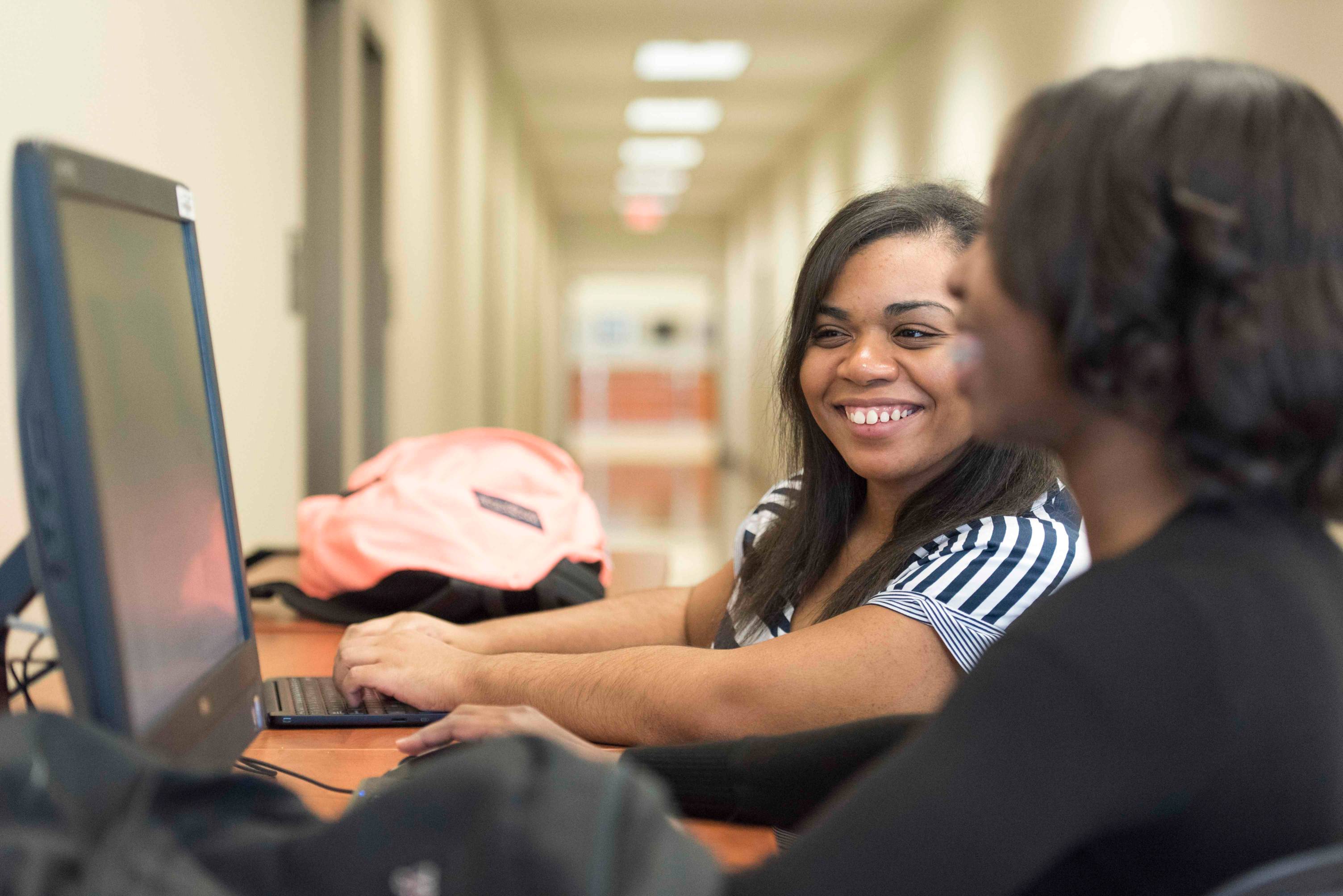 two students smile while sitting at a computer together