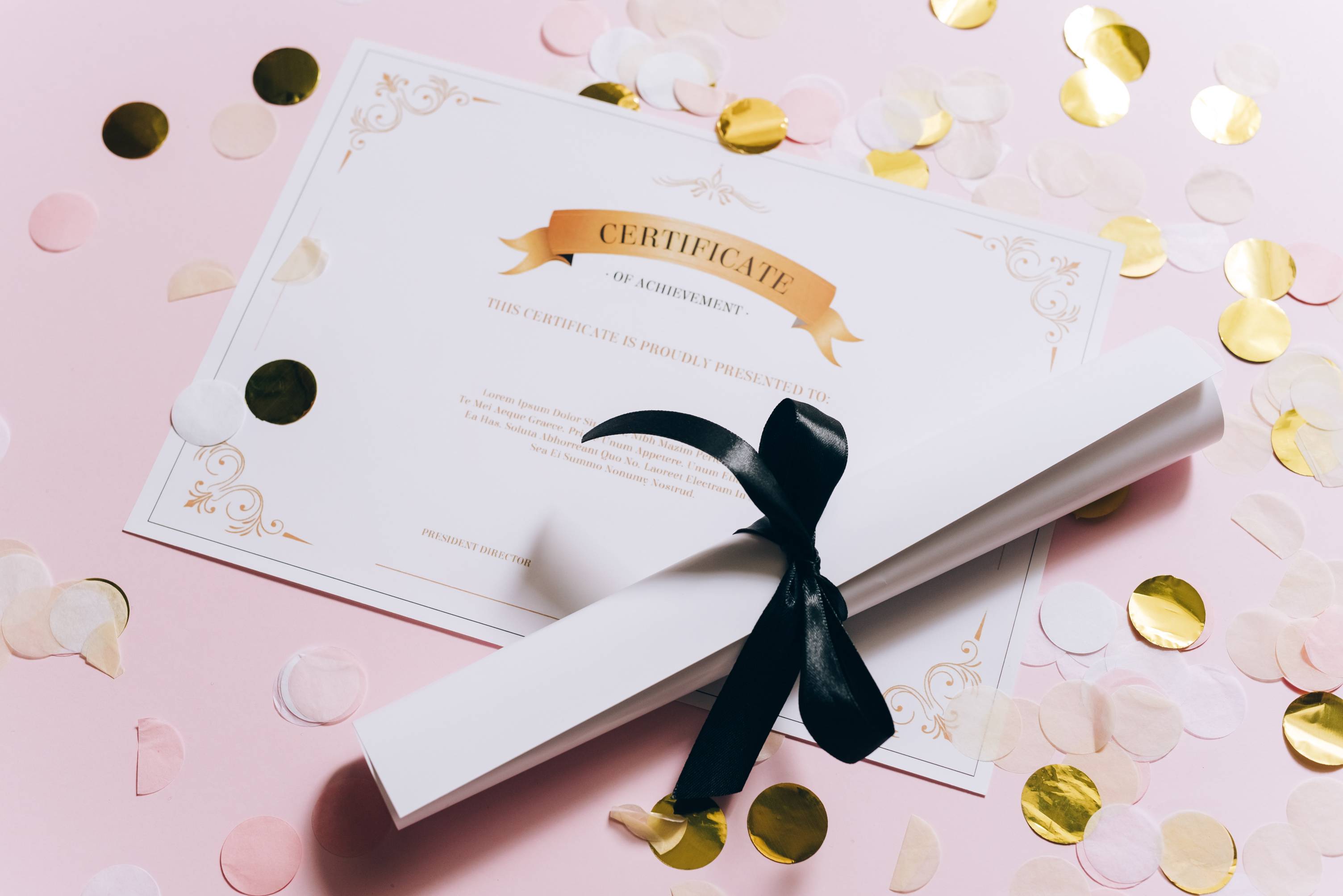 Certificate and scroll tied with ribbon on pink background