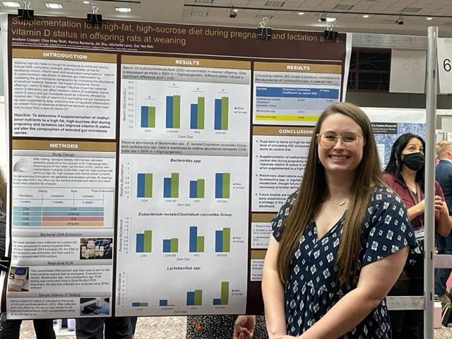 Analynn Cooper standing beside research poster in ballroom during Undergraduate Research Conference