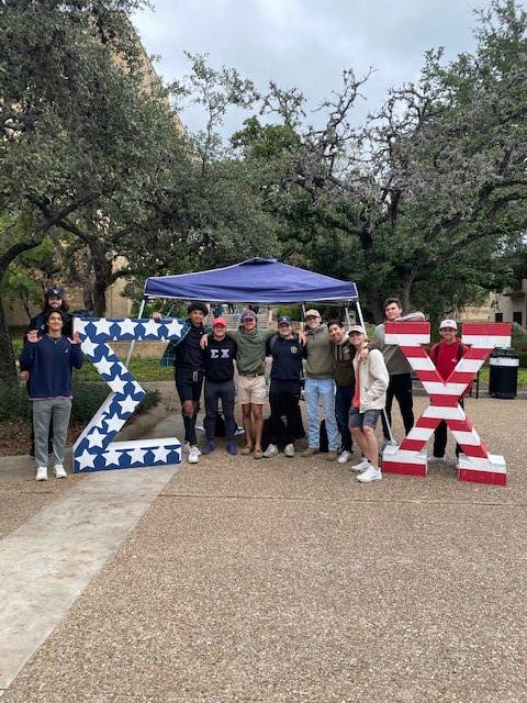 Men of Sigma Chi pose in the Quad underneath a canopy with their large letters on either side of the tent
